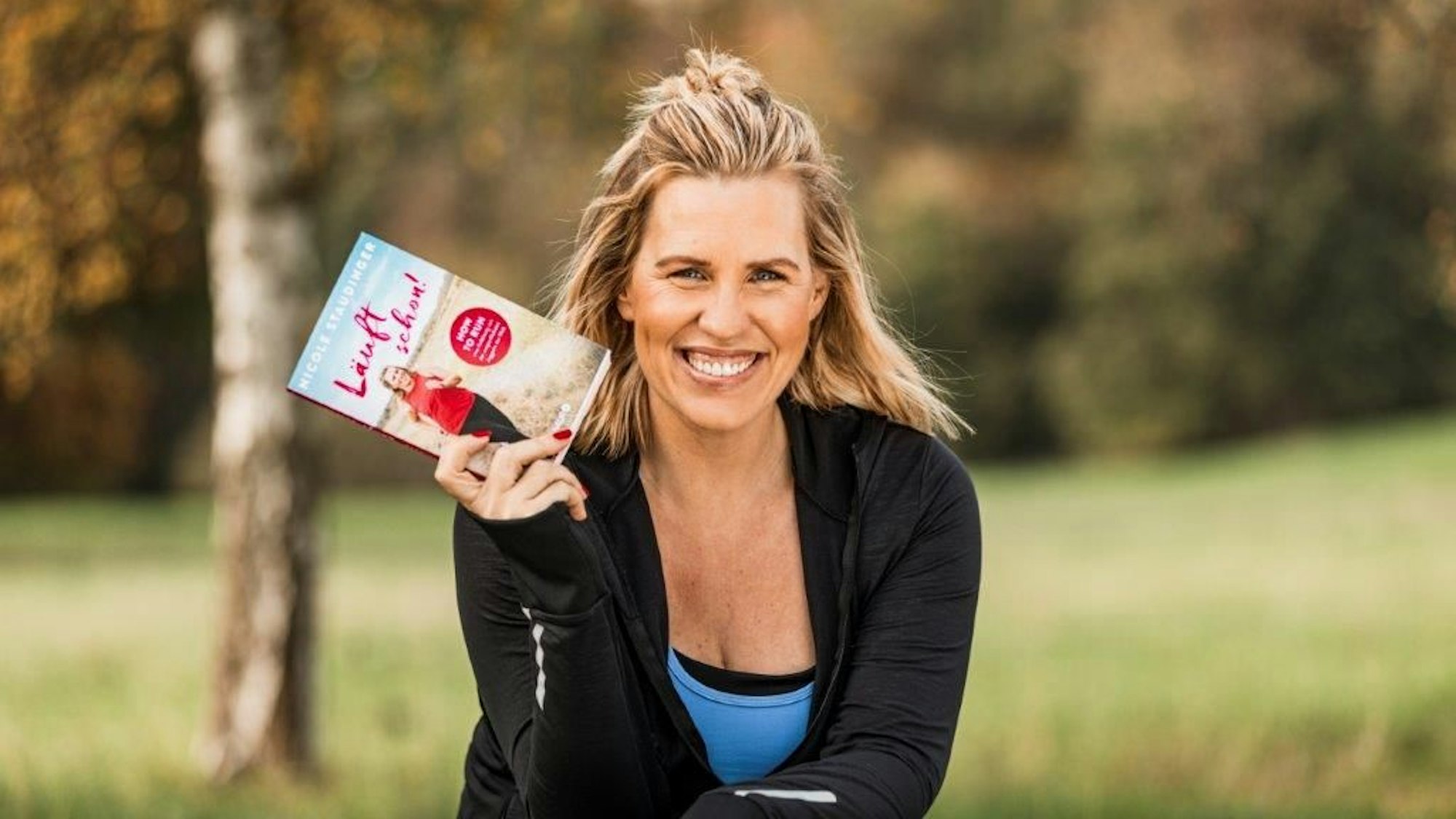 Nicole Staudinger sitzt mit ihrem Buch in der Hand in einem Park.