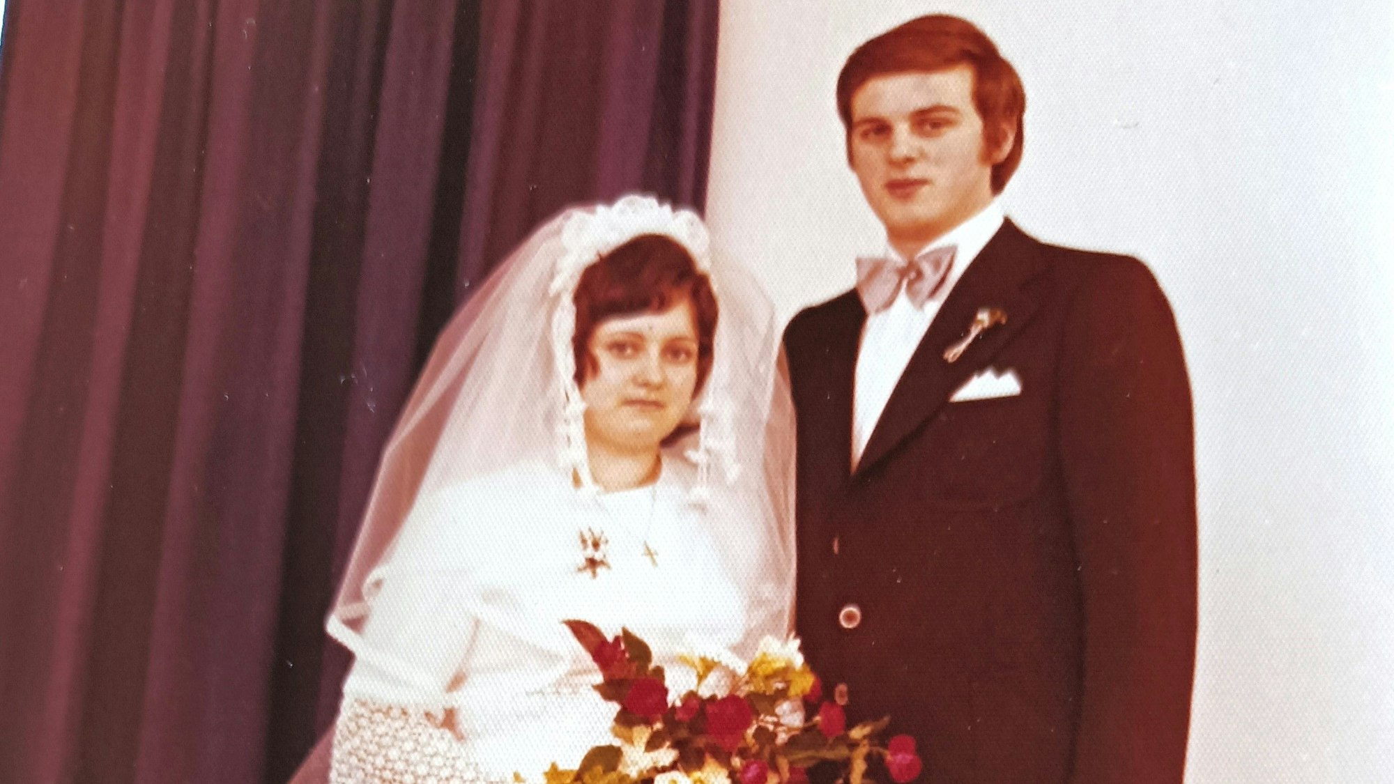 Gerda (l.) im Brautkleid und Peter im Anzug mit rosa Fliege.