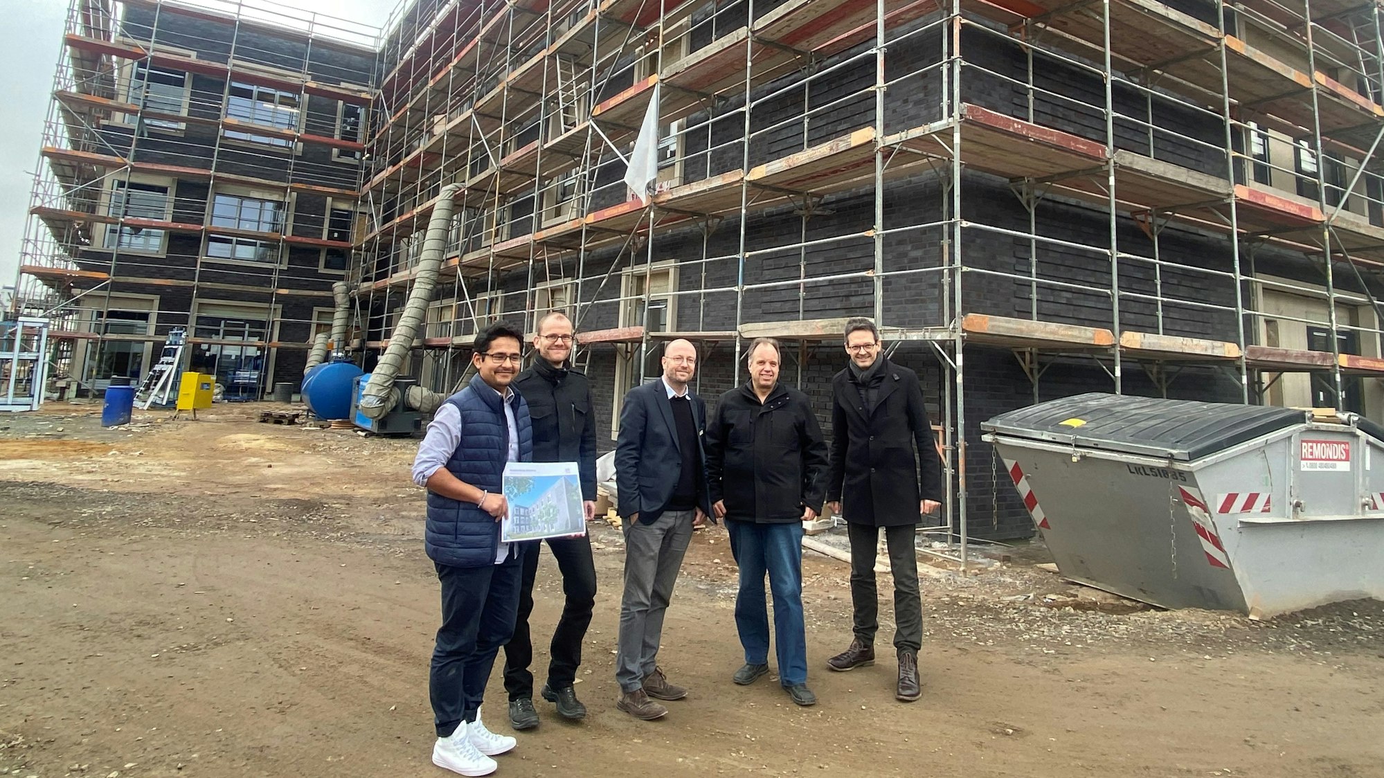 Fünf männliche Personen vor einem Gebäude, das ein Baugerüst um sich hat