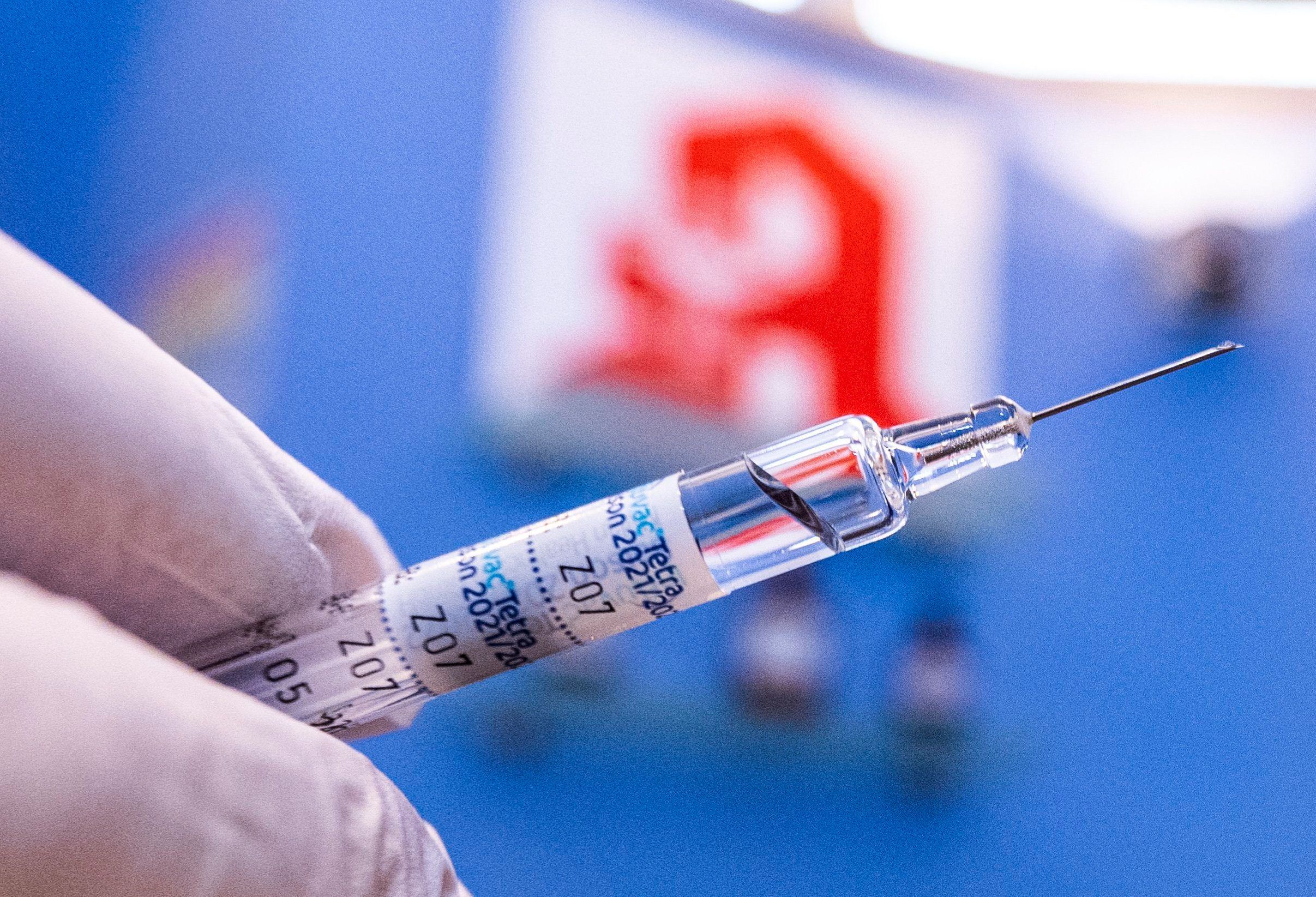 Dieses Symbolfoto zeigt, wie ein Apotheker eine Spritze mit Grippeschutzimpfstoff vor dem Logo der Apotheke in der Hand hält.
