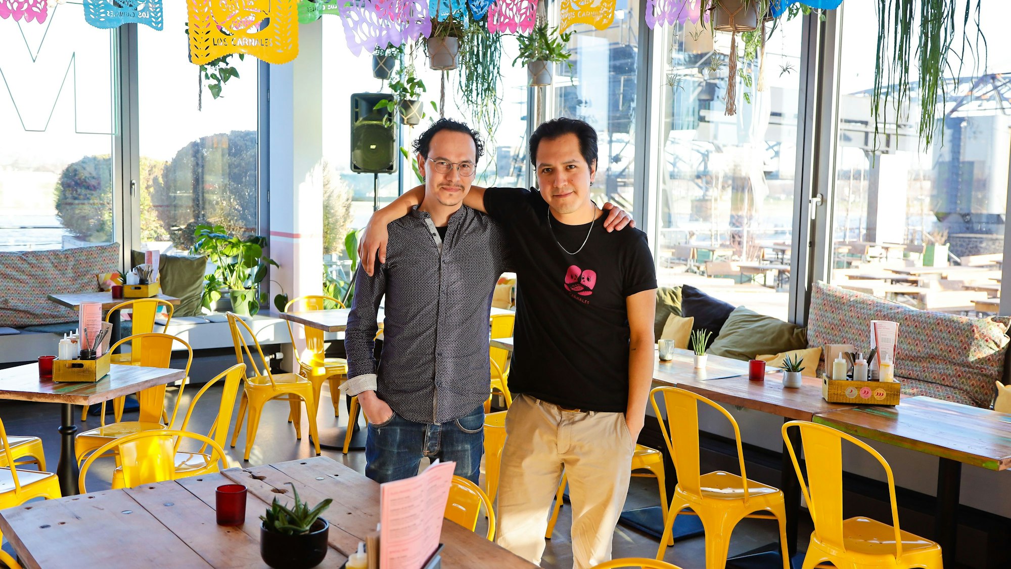 zwei Männer stehen Arm in Arm zwischen Tischen und Stühlen in einem Restaurant