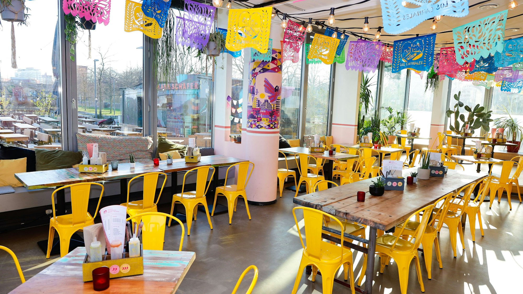 gelbe Stühle an Holztischen, an der Decke hängen bunte Girlanden