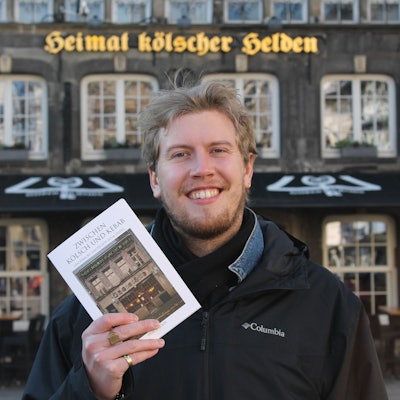 Ein Mann hält ein Buch in die Höhe mit dem Titel „Zwischen Kölsch und Kebab“.