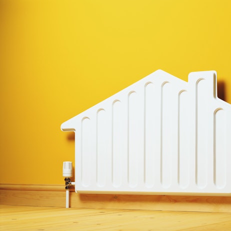 Ein Heizkörper in der Form eines Hauses steht vor einer gelben Wand.