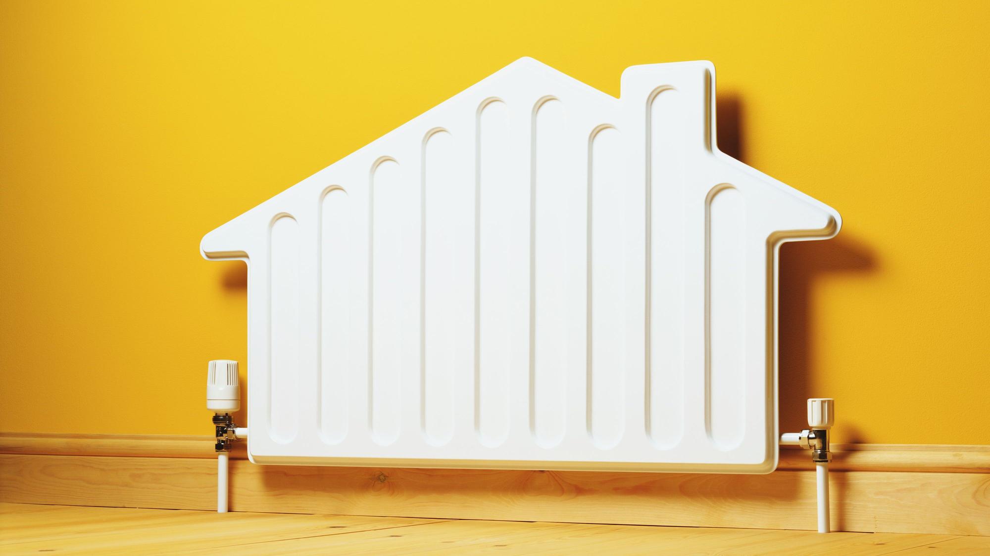 Ein Heizkörper in der Form eines Hauses steht vor einer gelben Wand.