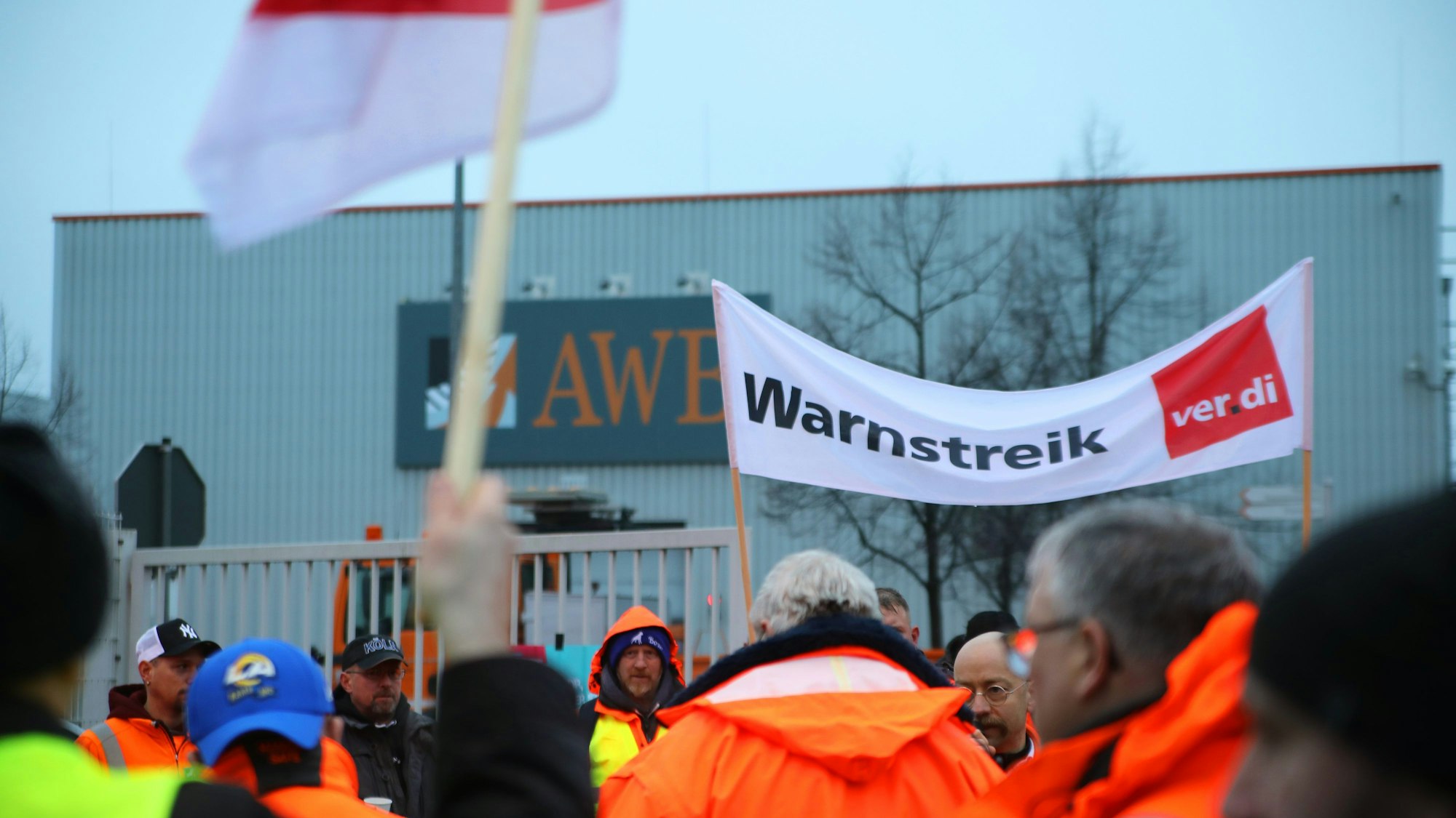 Streikende stehen mit einem Banner mit der Aufschrift „Warnstreik“ vor dem Werkstor der AWB Abfallwirtschaftsbetriebe.
