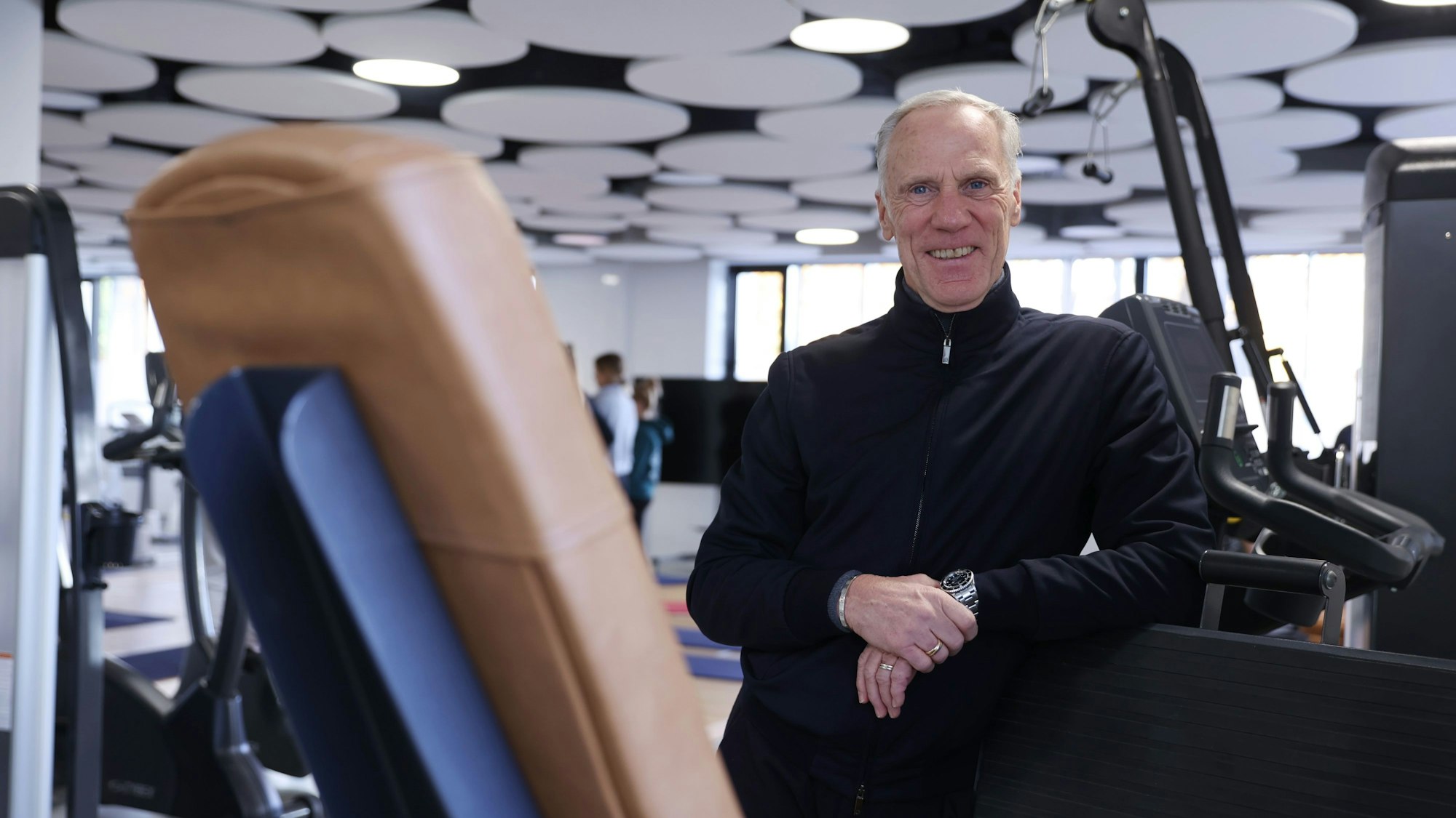 Ingo Froböse lehnt an einem Fitnessgerät in einem Fitnessstudio.
