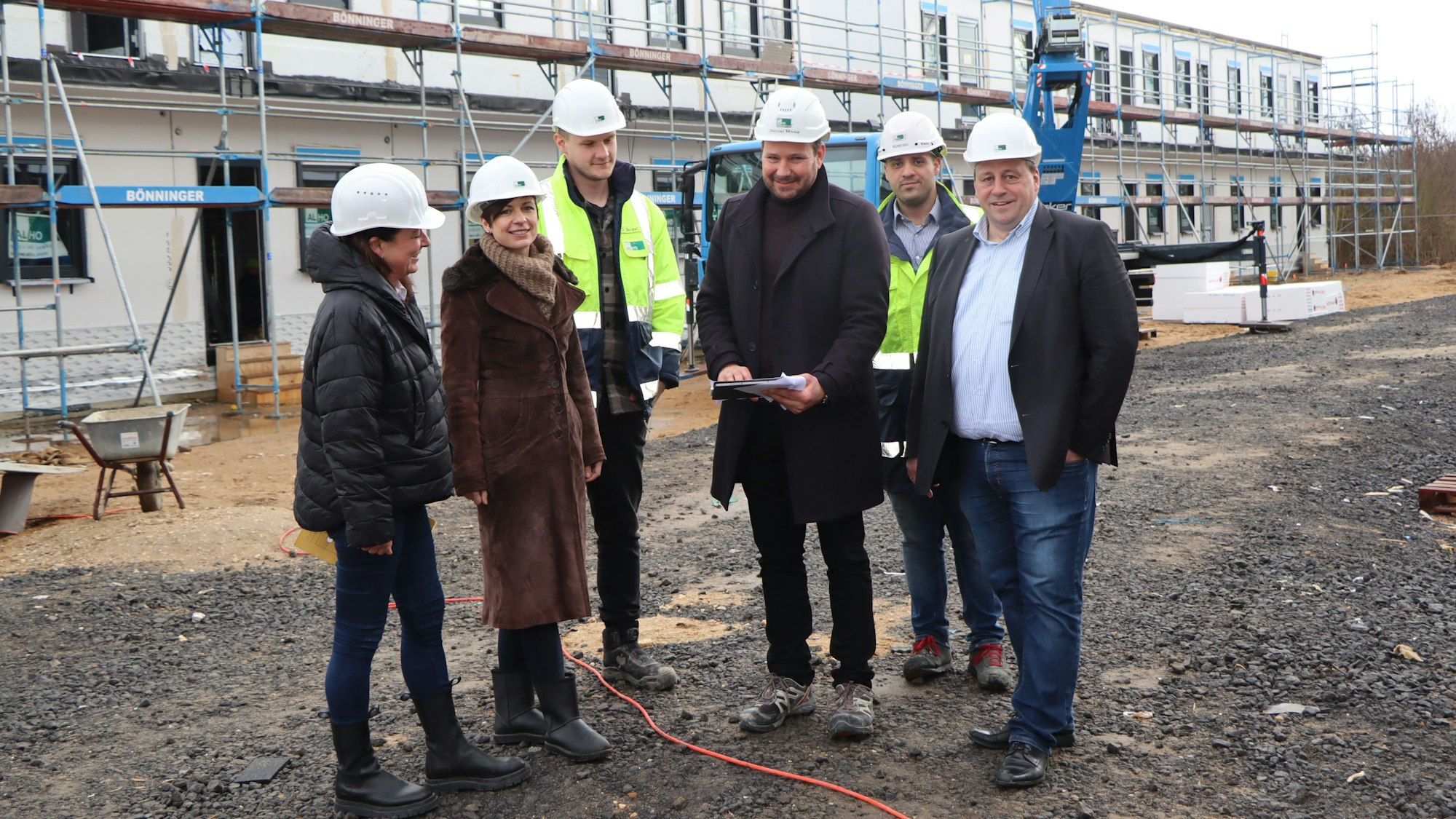 Diplomingenieur Daniel Maag und seine beiden Bauleiter erklärten Bürgermeisterin Carolin Weitzel, Gerd Schiffer und Kirsten Orth die Fortschritte auf der Baustelle. Sie stehen vor den eingerüsteten Unterkünften.
