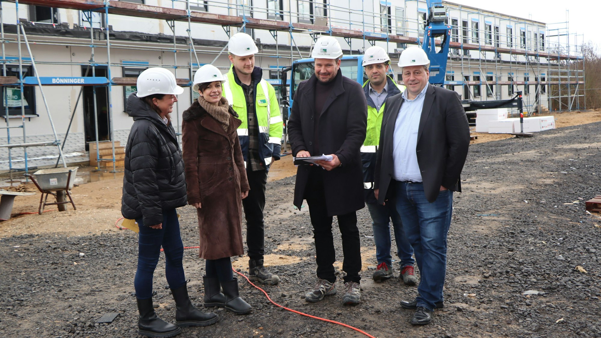 Diplomingenieur Daniel Maag und seine beiden Bauleiter erklärten Bürgermeisterin Carolin Weitzel, Gerd Schiffer und Kirsten Orth die Fortschritte auf der Baustelle. Sie stehen vor den eingerüsteten Unterkünften.