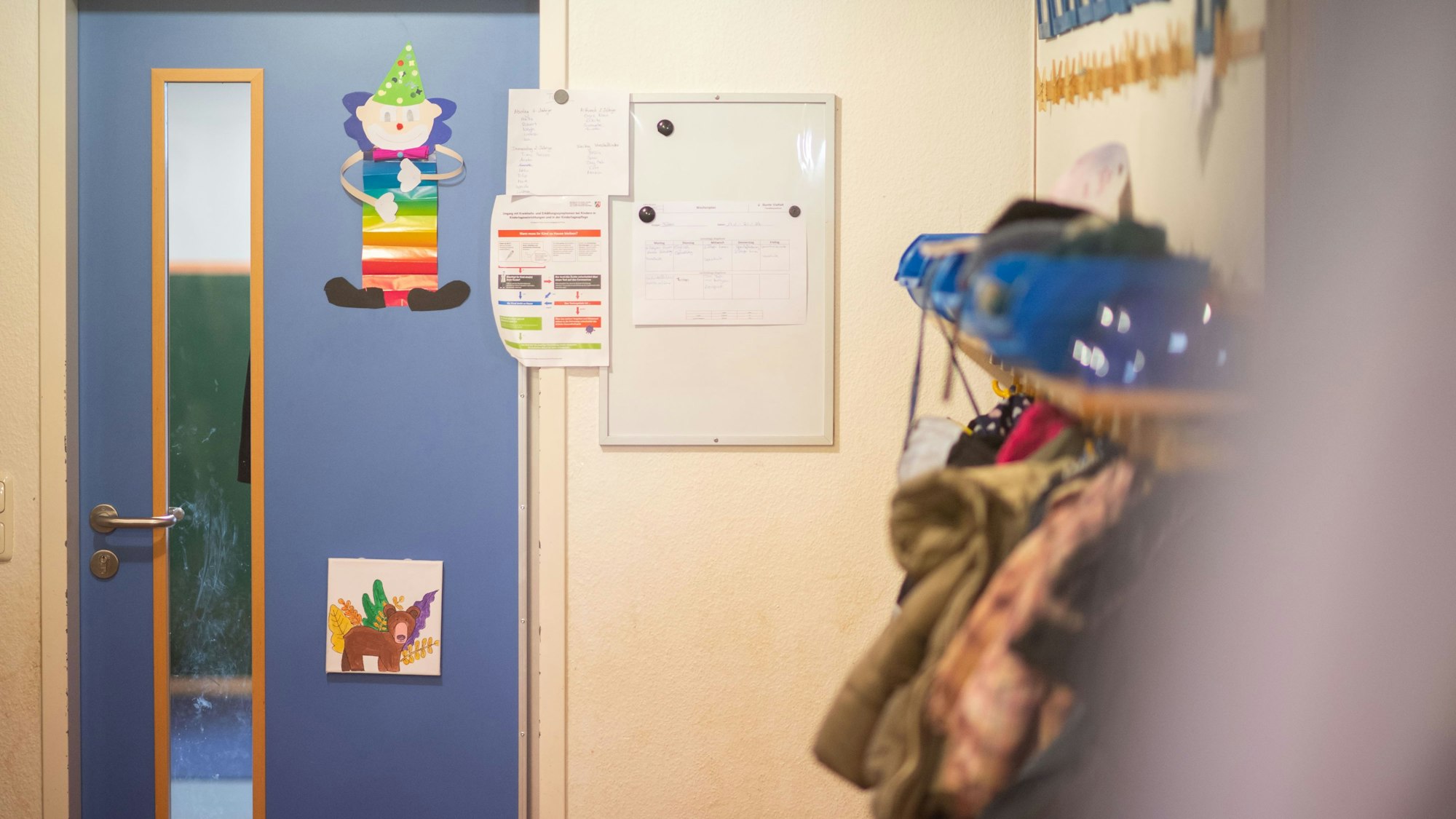 Kindergarten im Kreis Euskirchen. Tür mit Bildern, am rechten Rand hängen Jacken und Rucksäcke.