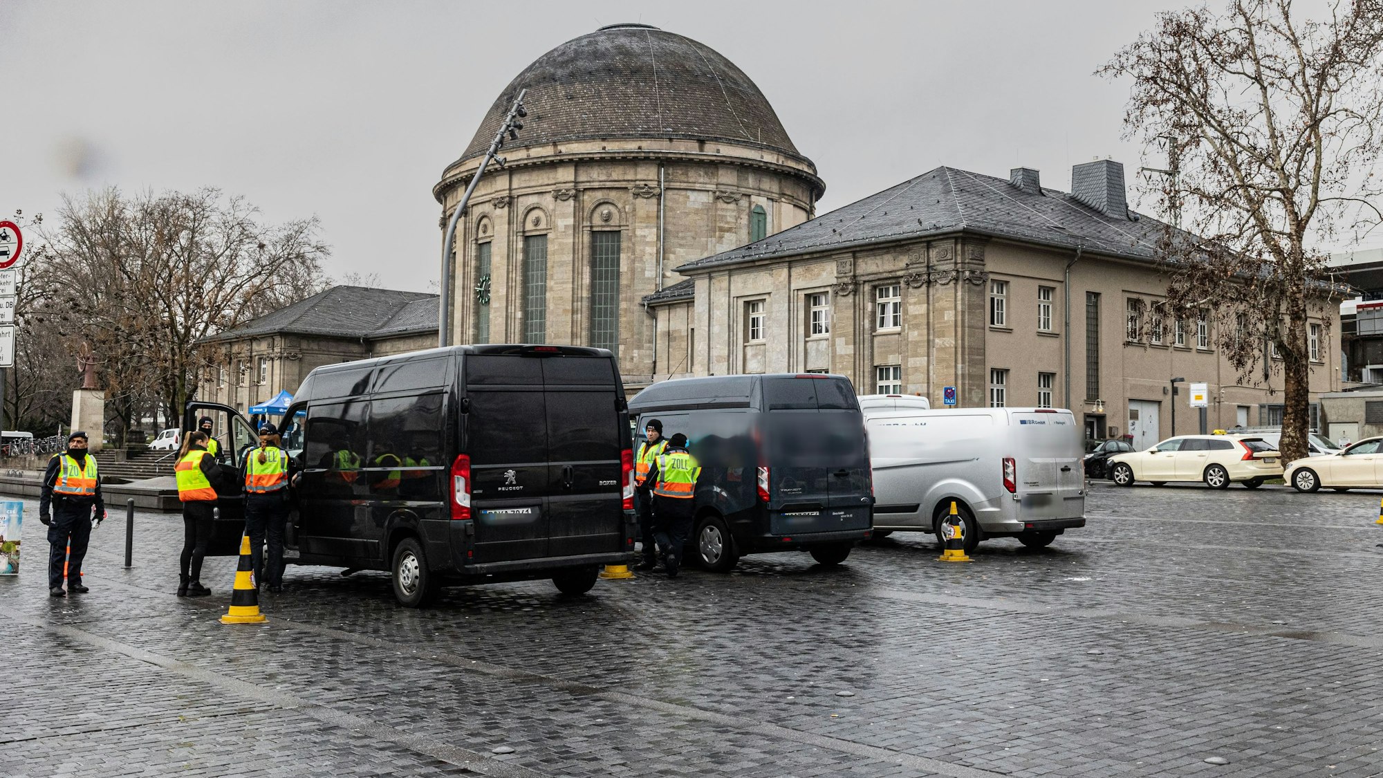 Zollbeamte in neongelben Westen und Kleintransportern vor dem Deutzer Bahnhof.