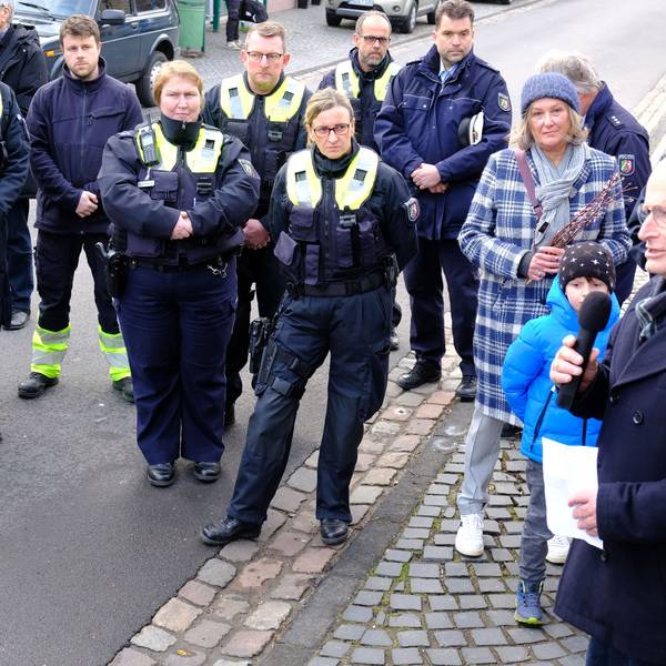 Polizistinnen und Polizisten sowie Menschen in ziviler Kleidung stehen auf einer Straße und hören Michael Heinen zu.