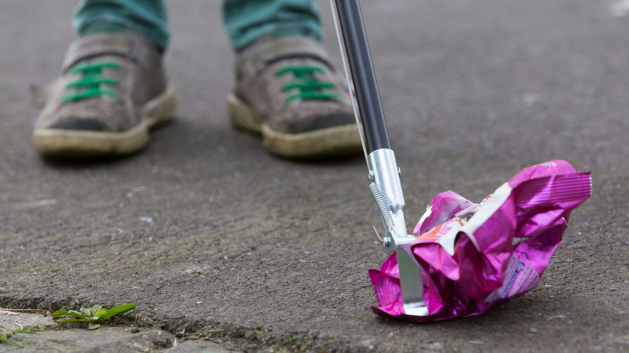 Müll wird mit einer Müllgreifzange vom Boden aufgehoben.