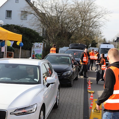 Menschen in Warnwesten nehmen Spenden in Kartons entgegen, die mit Autos in einem Drive-in angeliefert werden.