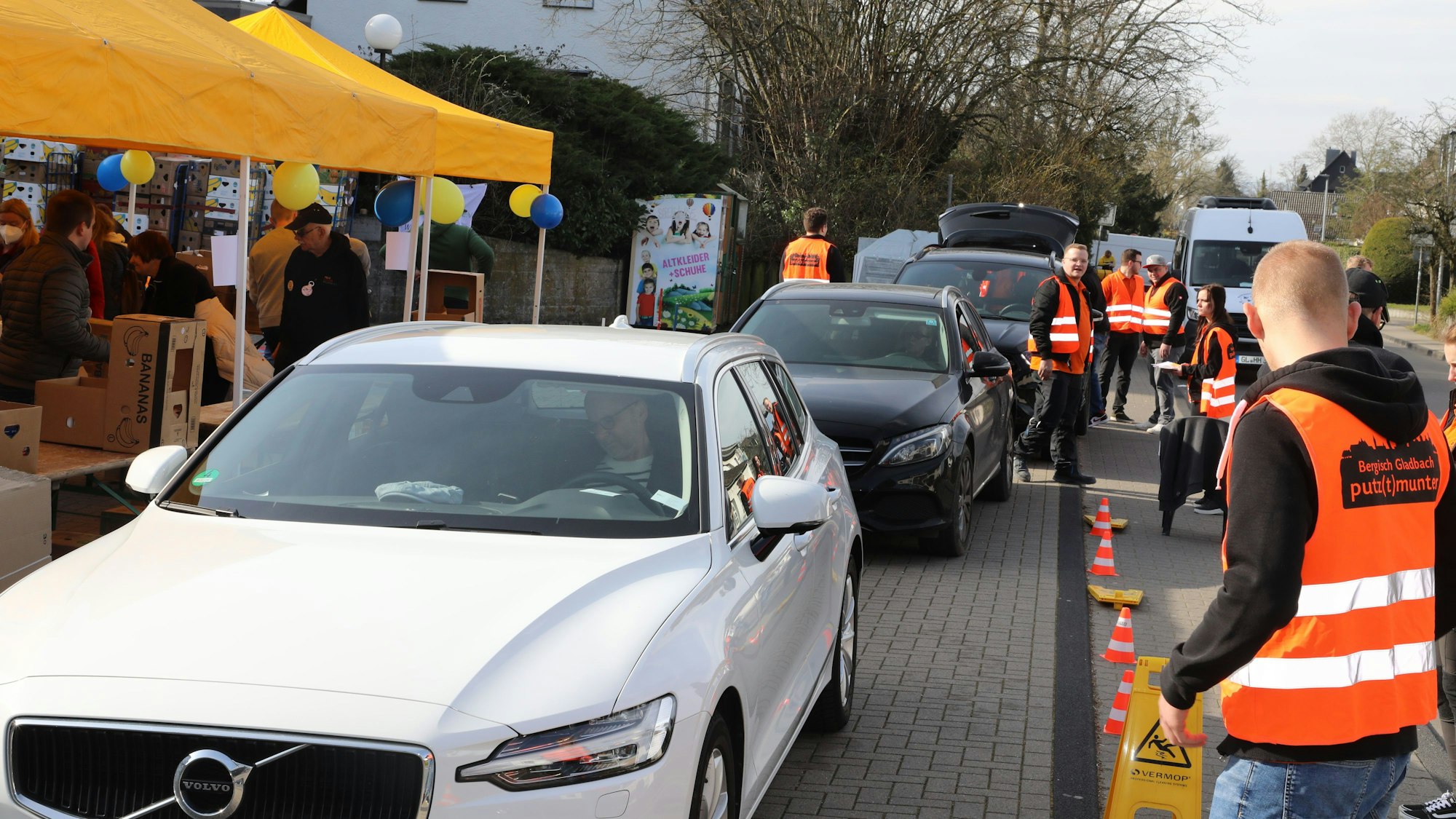 Menschen in Warnwesten nehmen Spenden in Kartons entgegen, die mit Autos in einem Drive-in angeliefert werden.