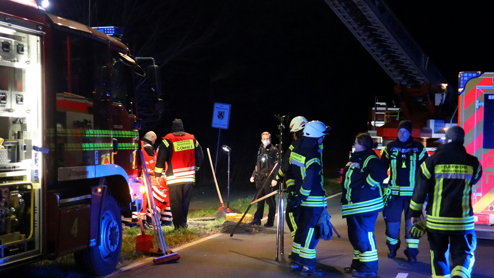An einem nächtlichen Einsatzort sind Feuerwehrleute im Einsatz. Ein offener Gullydeckel ist hell angestrahlt.