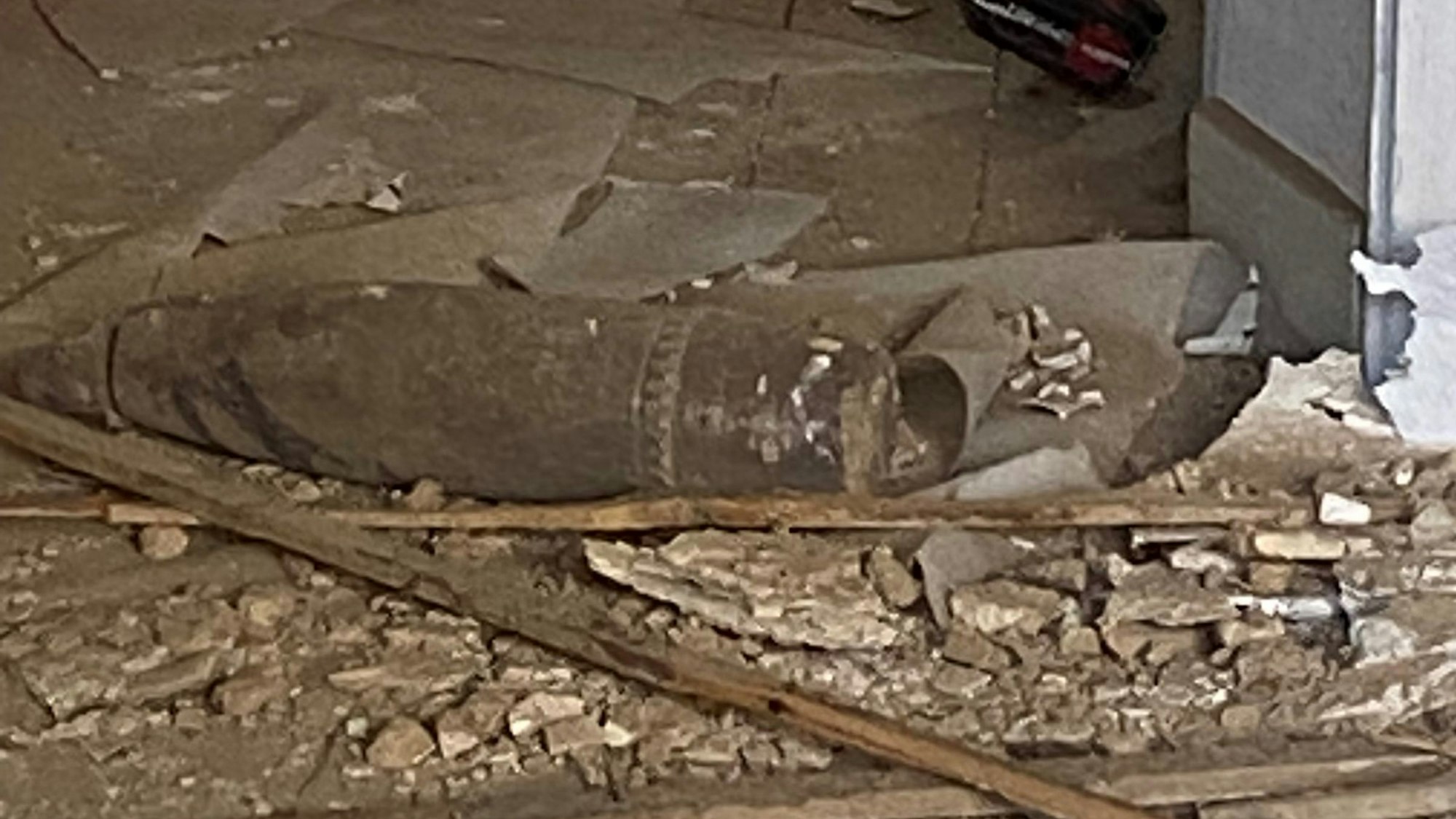 Zwischen Bauschutt und Holzleisten liegt eine lange, zylinderförmige Bombe.