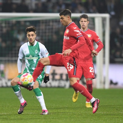 Auf einem Fußballplatz stehen zwei Spieler von Leverkusen und ein Spieler von Bremen, die um den Ball kämpfen.