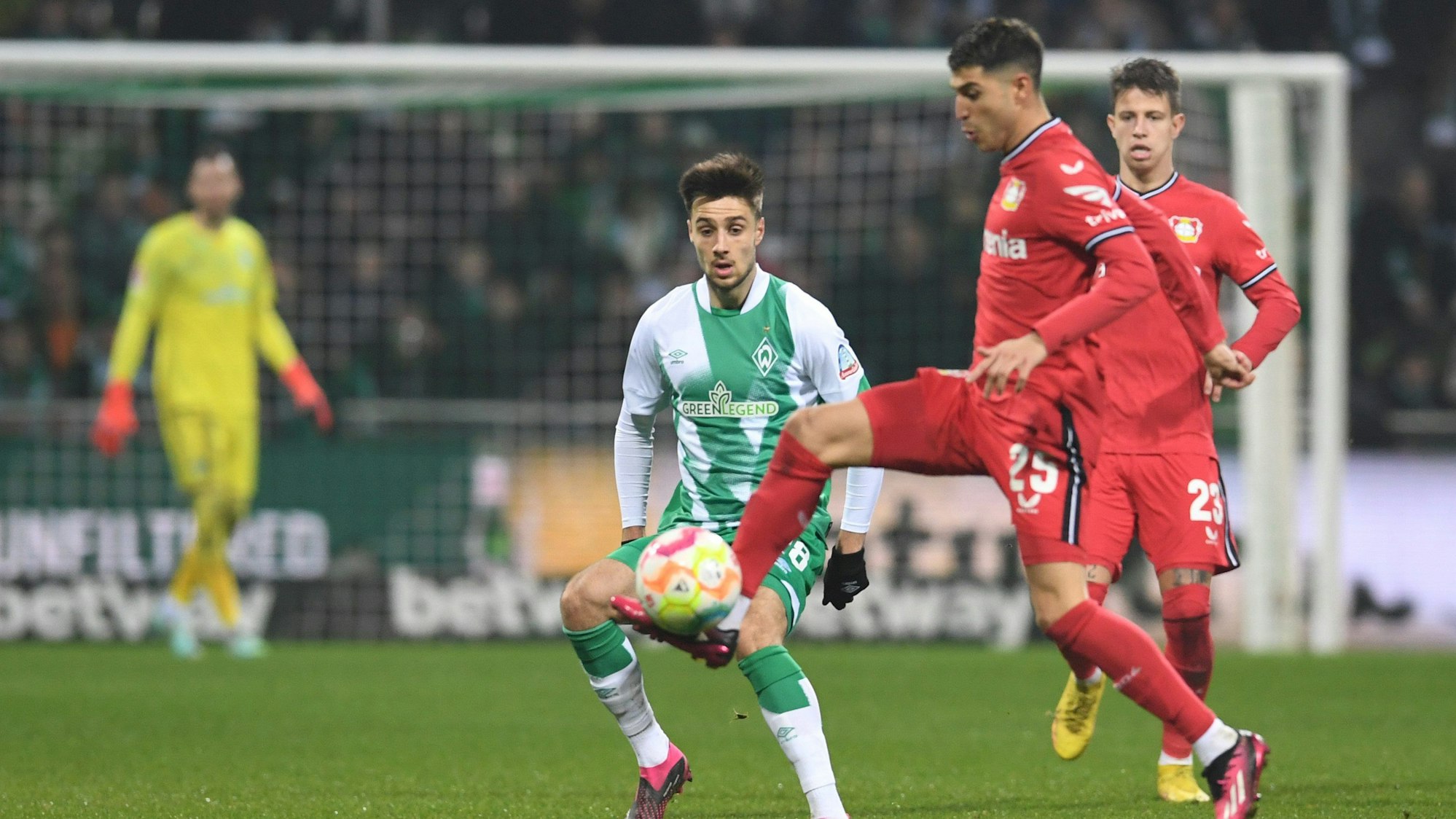 Auf einem Fußballplatz stehen zwei Spieler von Leverkusen und ein Spieler von Bremen, die um den Ball kämpfen.
