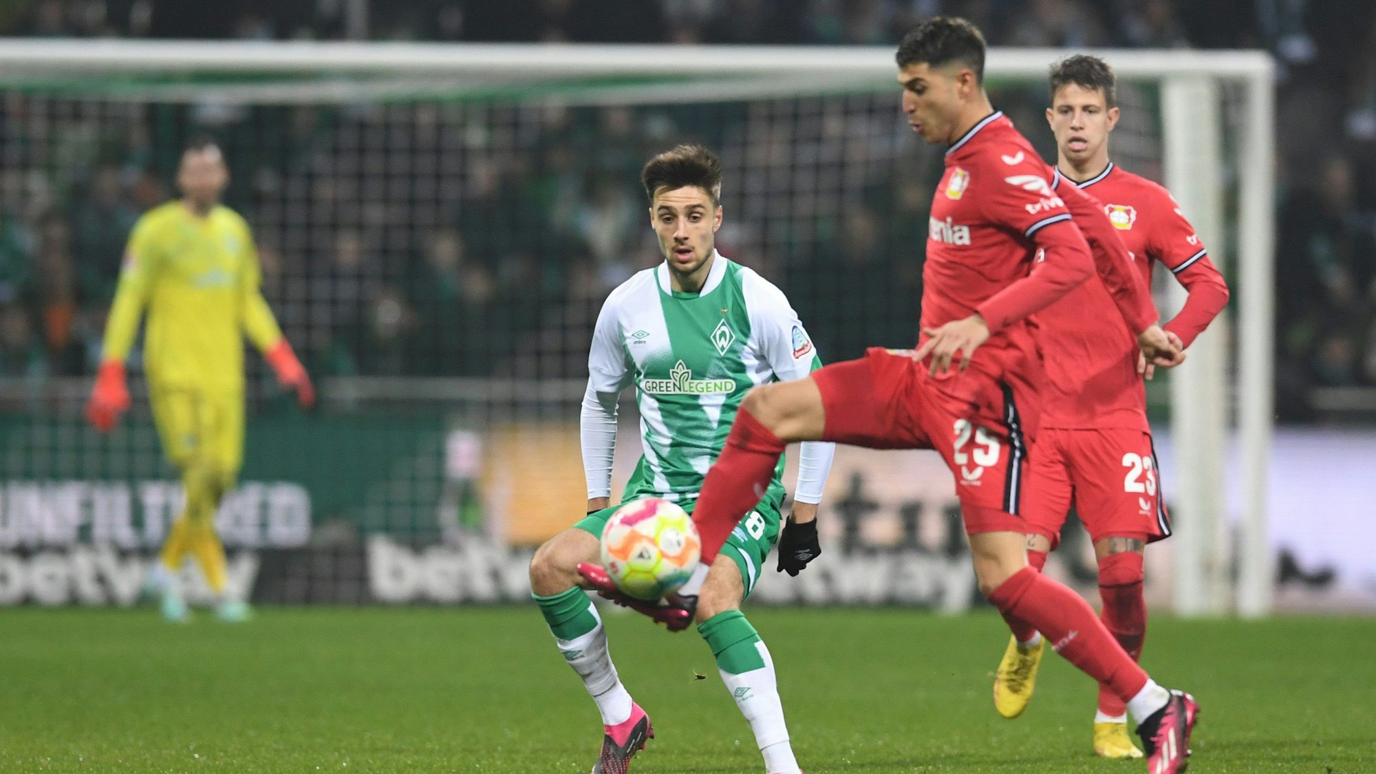 Auf einem Fußballplatz stehen zwei Spieler von Leverkusen und ein Spieler von Bremen, die um den Ball kämpfen.