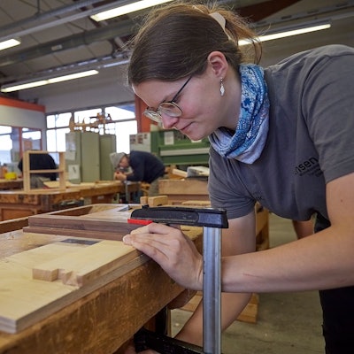 An einer Werkbank arbeitet eine junge Auszubildende, die das Tischlerhandwerk lernt.