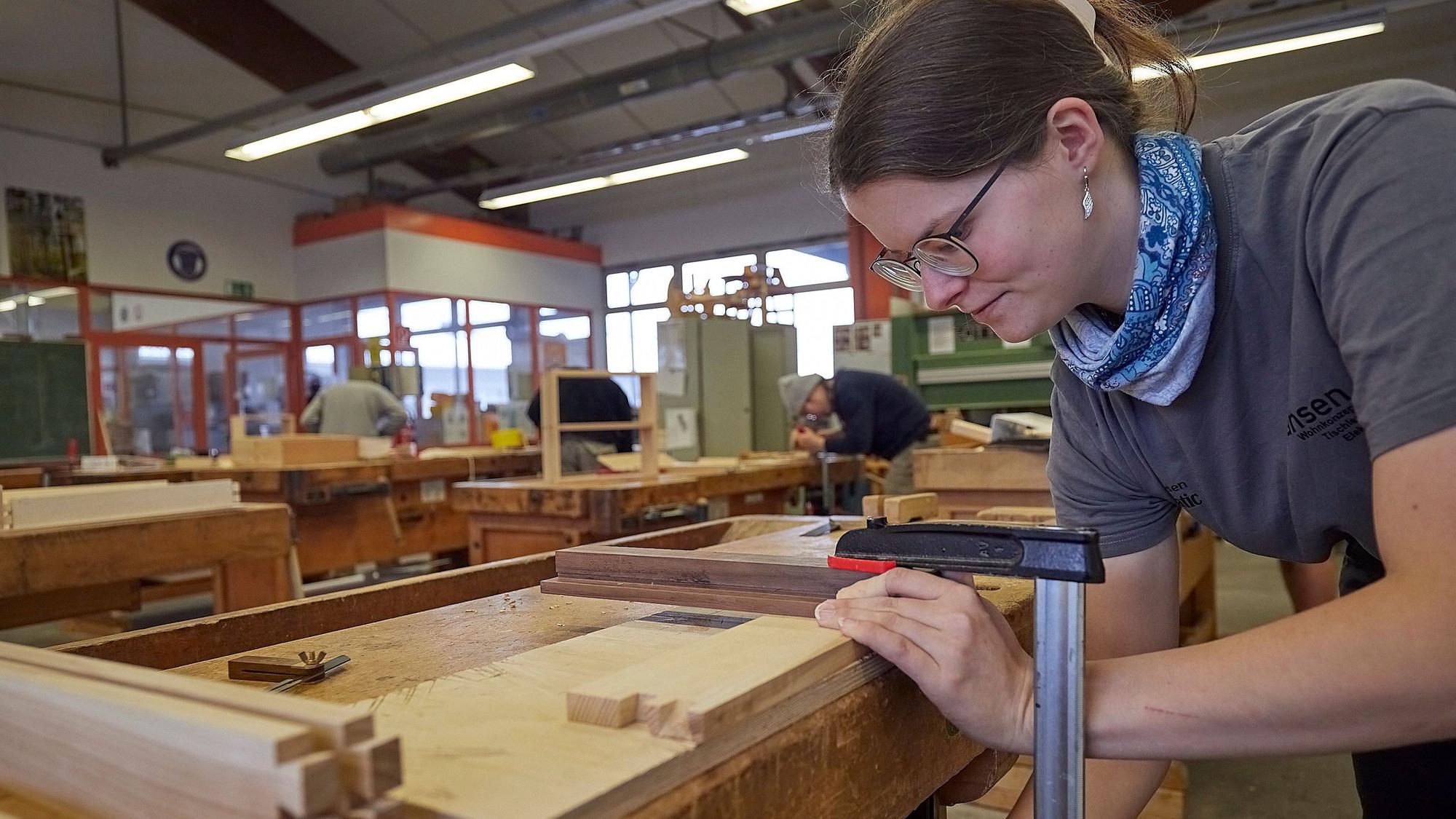An einer Werkbank arbeitet eine junge Auszubildende, die das Tischlerhandwerk lernt.