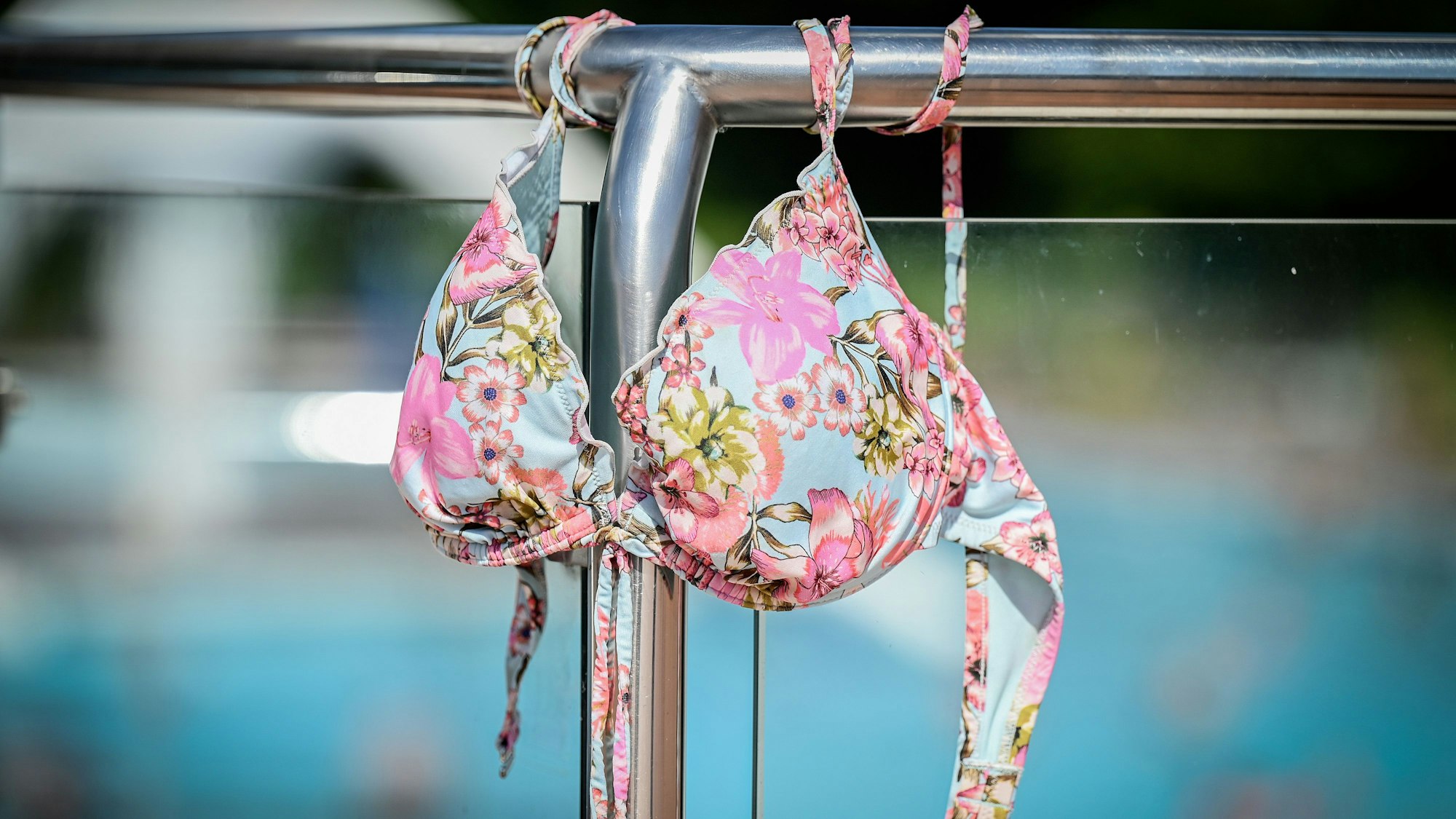Ein Bikinioberteil hängt an einem Schwimmbad-Geländer.