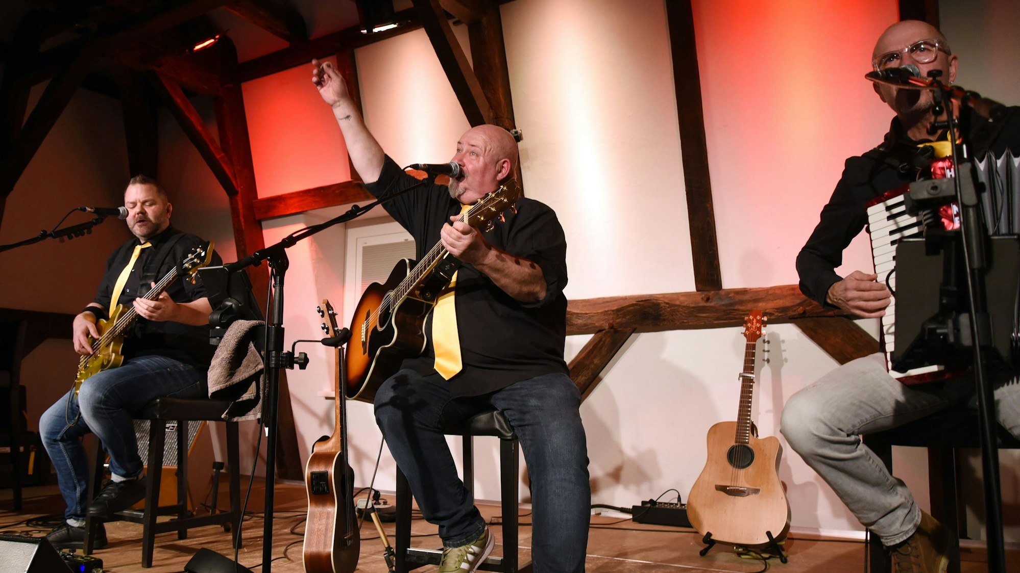 Drei Musiker der Gruppe Goldene Reiter sitzen auf Barhockern auf der Bühne und musizieren.