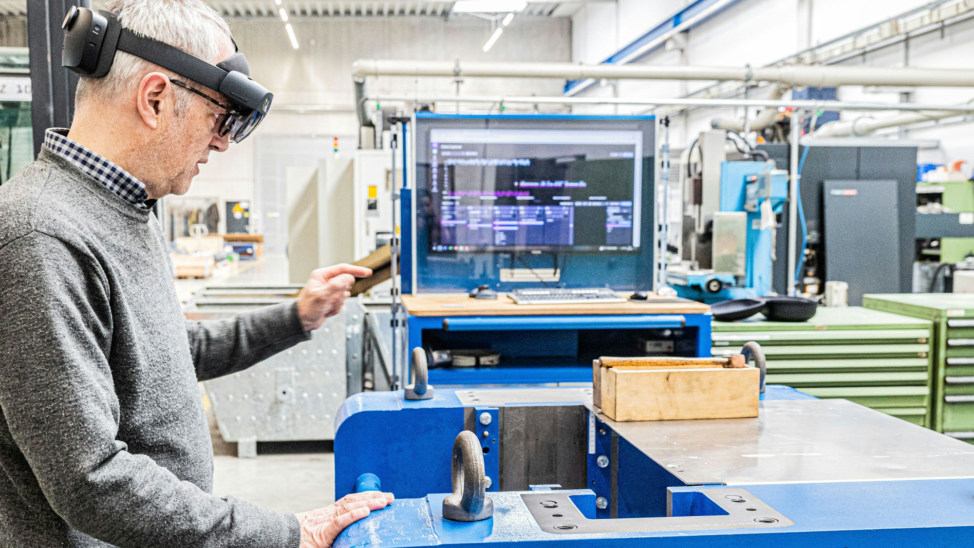 Ein Mann steht an einem Arbeitsplatz in einer Fabrikhalle. Er trägt eine Datenbrille.