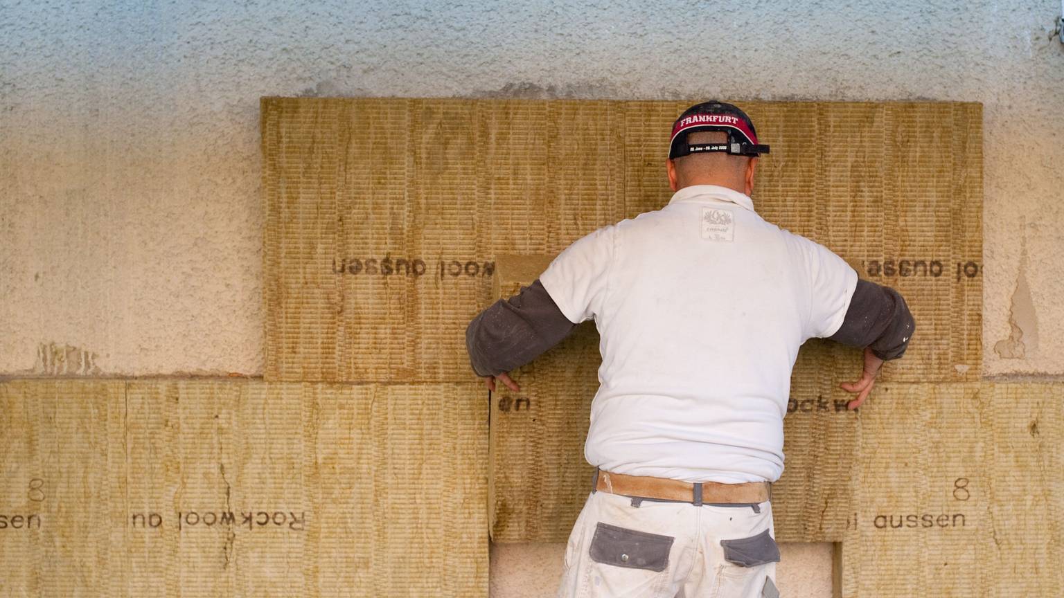 Ein Mann bringt Dämmmaterial an einer Wand an.