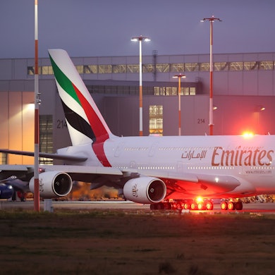 Ein Airbus A380 der arabischen Fluggesellschaft Emirates rollt zur Start- und Landebahn. Im Hintergrund ist ein großer Hangar zu sehen.