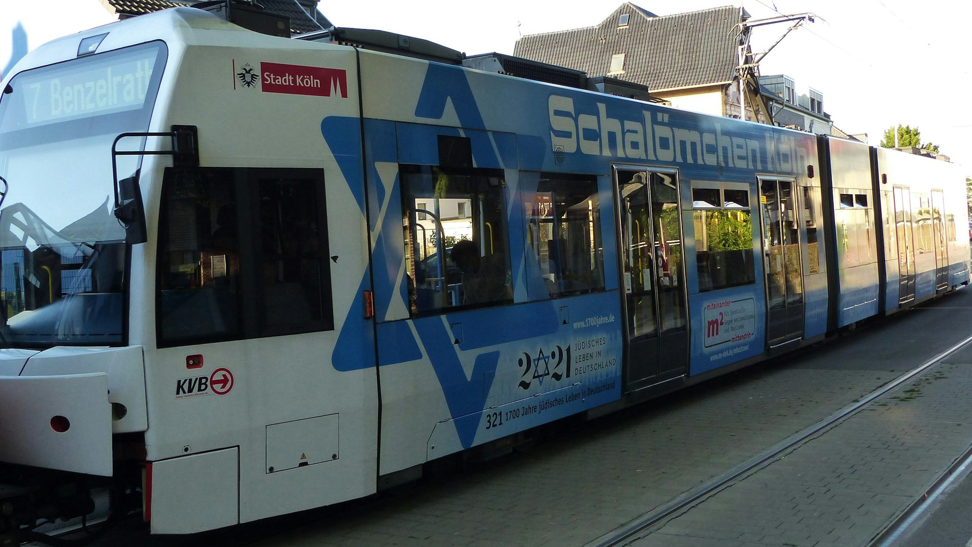 Durch eine Frechener Straße fährt eine KVB-Straßenbahn der Linie 7 mit blau-weißem Schriftzug "Schalömchen Köln".