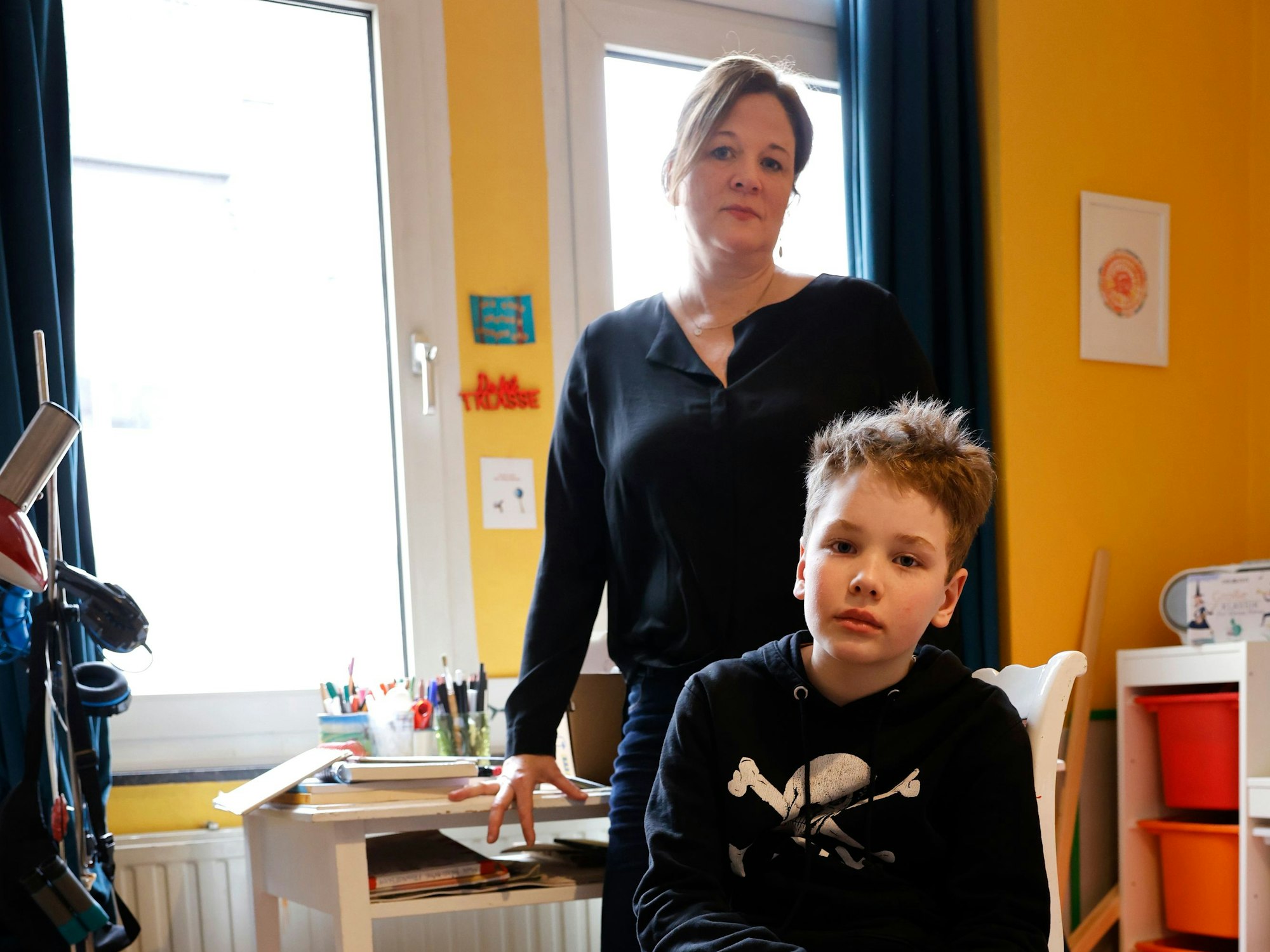 Man sieht Titus und auf einem Stuhl sitzend, seine Mutter steht hinter ihm.