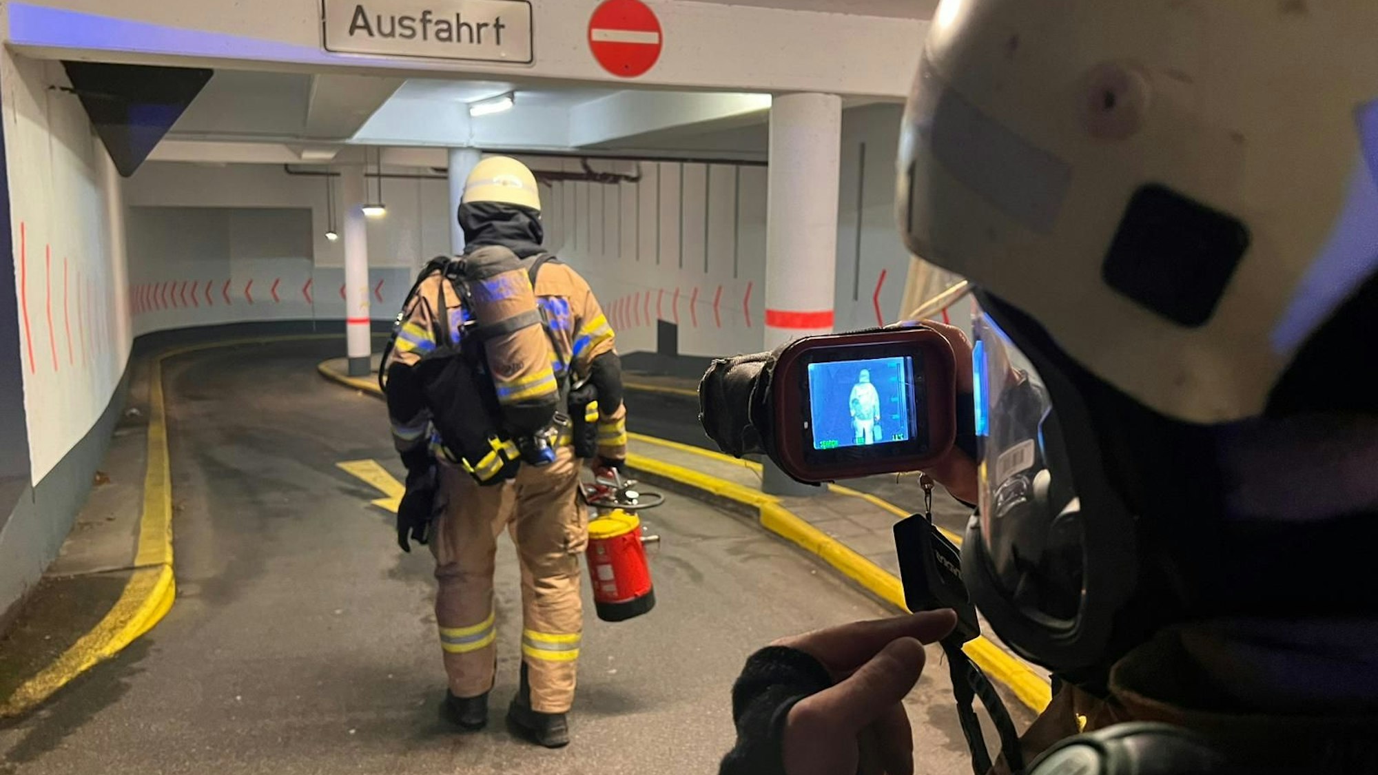Ein Feuerwehrmann geht unter Atemschutz in eine Tiefgarage, ein weiterer folgt ihm mit einer Wärmebildkamera.