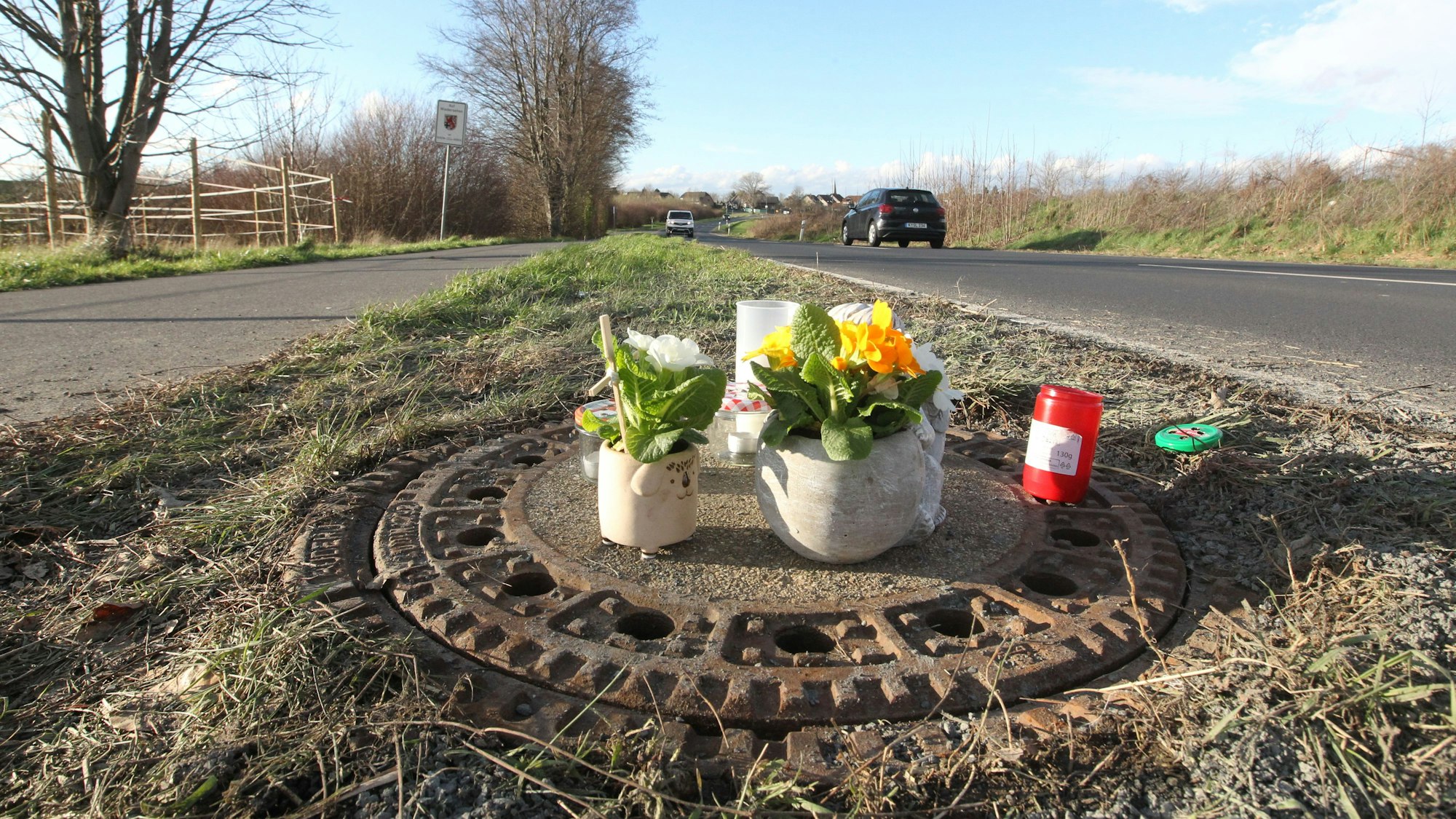 Blumen und Kerzen stehen auf einem Gullydeckel.