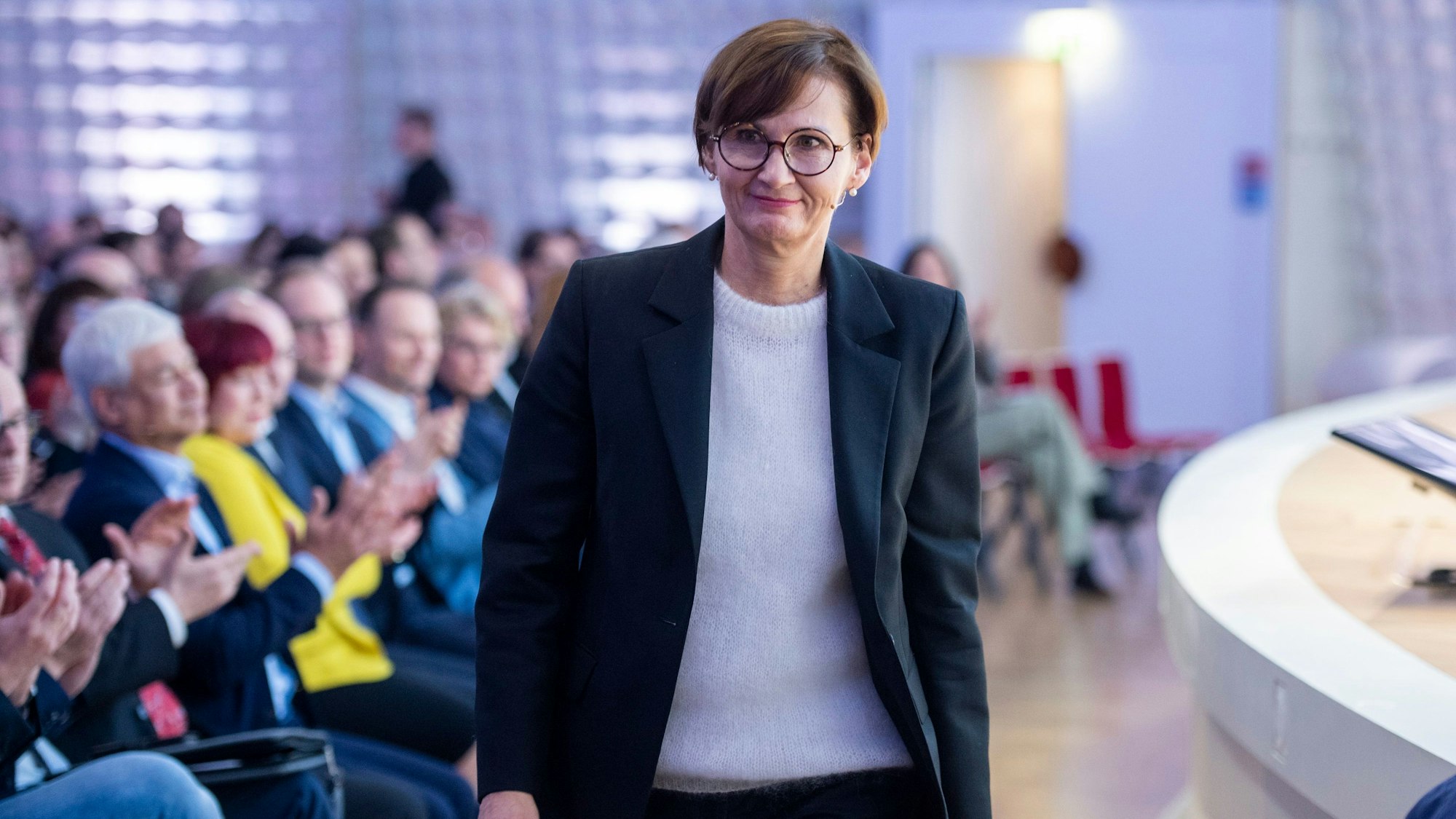 Man sieht die Ministerin, wie sie an einer Bühne entlangläuft, im Hintergrund klatschendes Publikum.