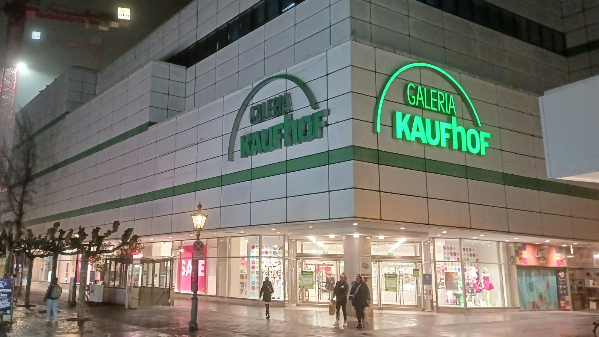 Die Front der Galeria Kaufhof an der Siegburger Kaiserstraße am Abend. Ein Schriftzug leuchtet, ein anderer ist dunkel.