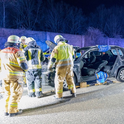 Feuerwehrleute stehen an einem aufgeschnittenen Auto auf der Autobahn. im Hintergrund stehen ein Feuerwehrfahrzeug und ein Polizeiwagen.