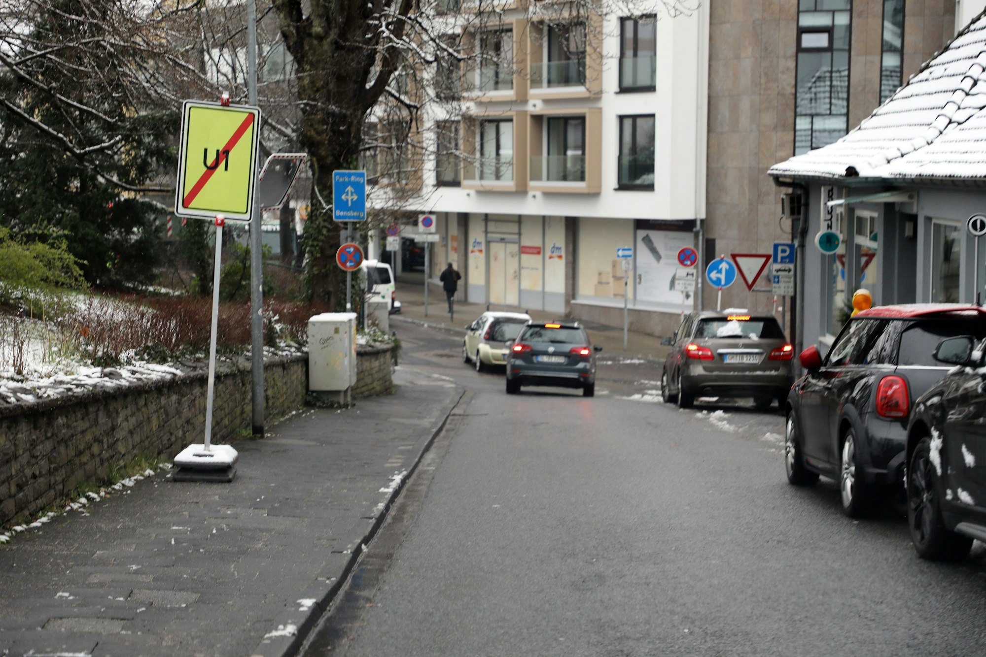 Ein Schild neben der Straße zeigt das Ende einer Umleitung an. Autos fahren auf der Straße bergab und geradeaus über eine Kreuzung.