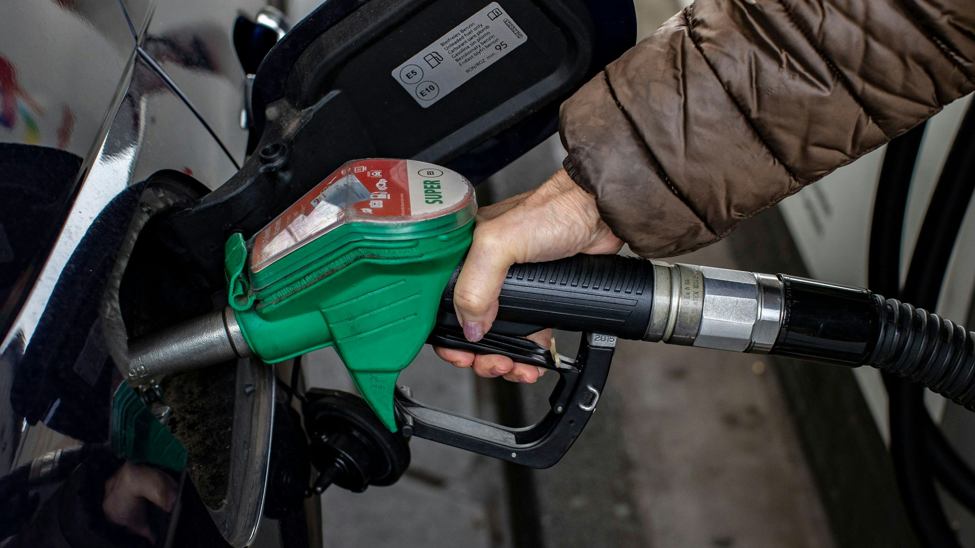 Eine Frau tankt ihr Fahrzeug, sie hält die Zapfpistole an einer Tankstelle fest.