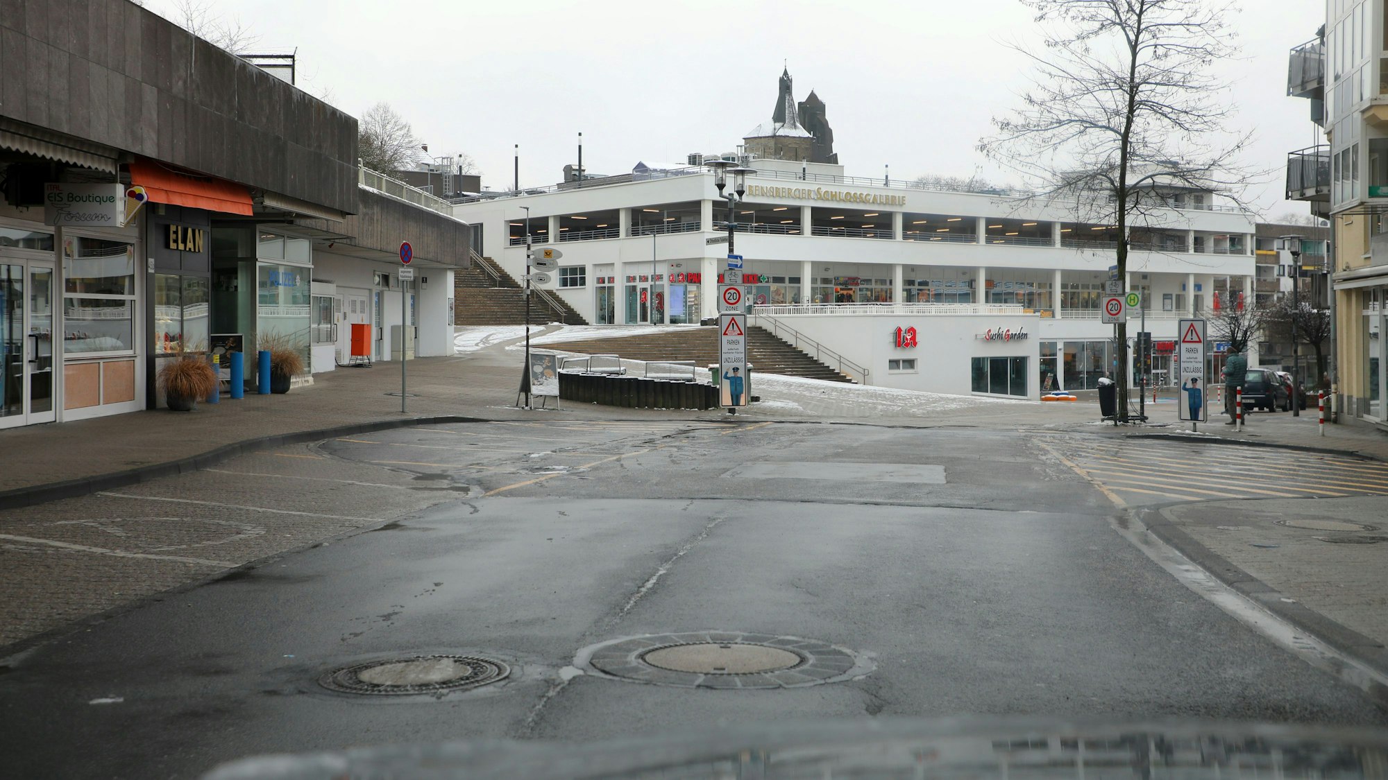 Durch die Frontscheibe eines Autos ist die Schloßstraße und an ihr das Einkaufszentrum Schlossgalerie zu sehen. Zahlreiche Parktaschen neben der Fahrbahn sind frei.