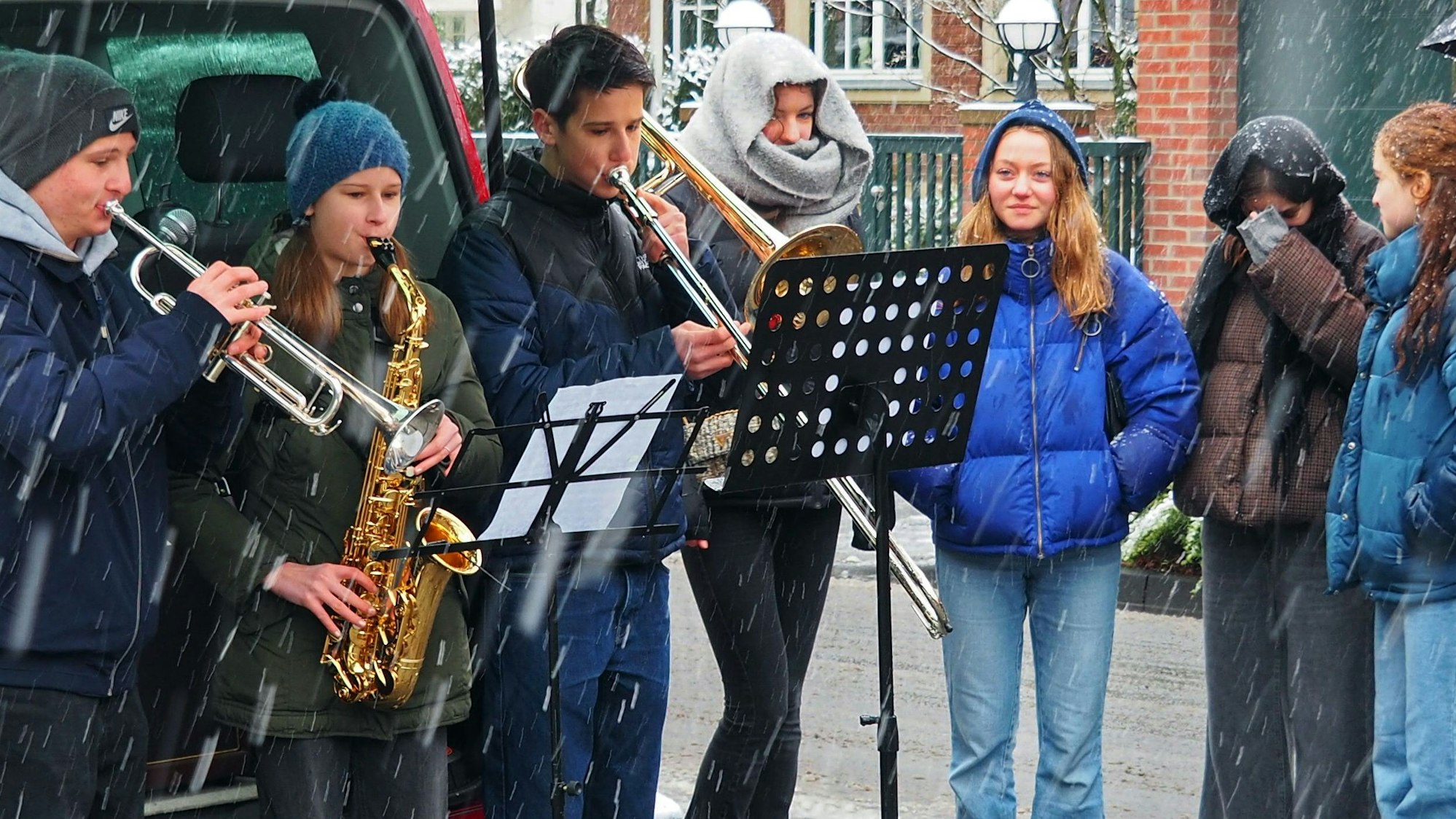 Kinder, die mit zwei Trompeten und einem Saxophon vor einem Notenständer stehen und musizieren