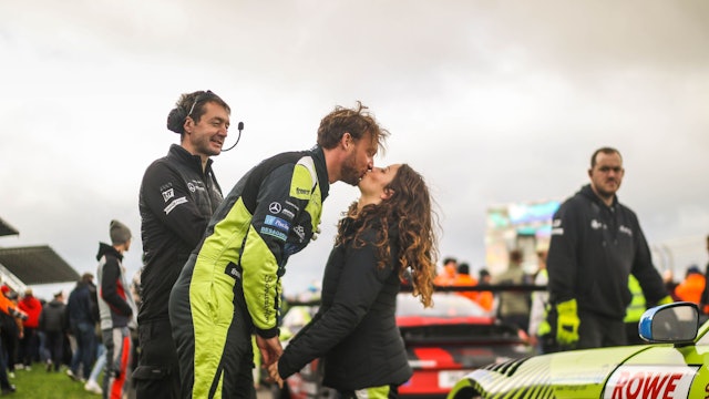 Die Rennfahrer Schreiner und Terting küssen sich neben den Autos.