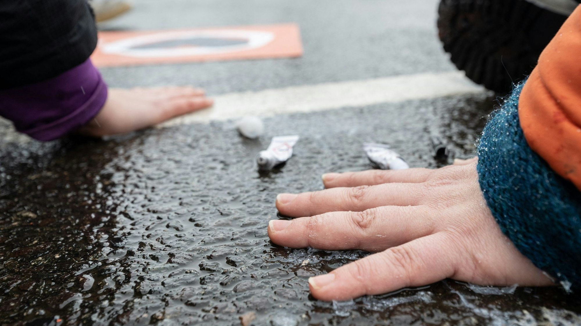 Klimaschutzaktivisten der „Letzten Generation“ kleben sich mit Sekunden kleben auf dem Asphalt einer Straße fest. Im Hintergrund stehen Autofahrer deswegen im Stau.