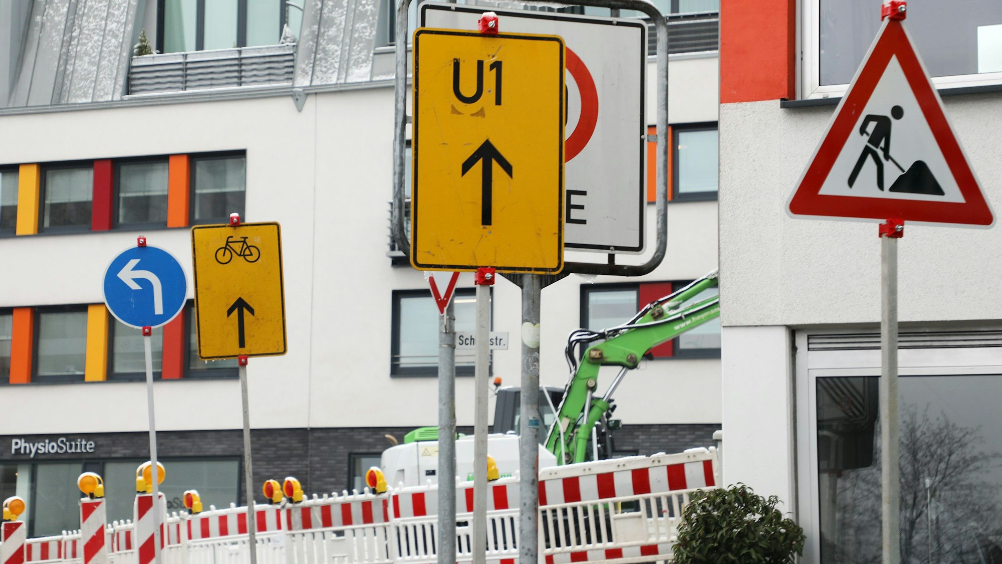 Zwei Umleitungsschilder weisen nach geradeaus, ein weißer Richtungspfeil auf blauem Grund hingegen nach links. Zudem ist ein Baustellenschild zu sehen.