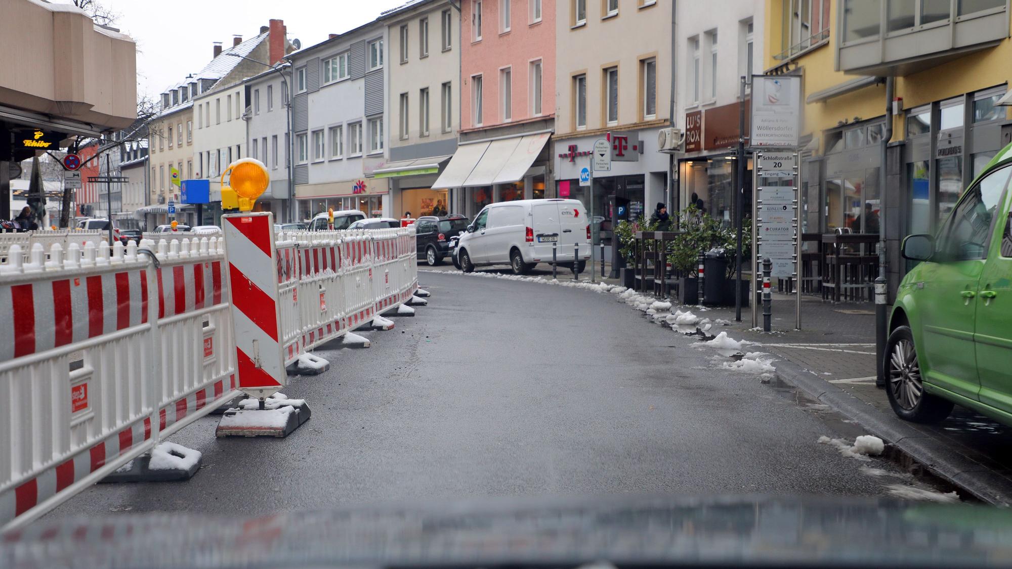 Links der Straßenfahrbahn sind Baustellenbaken an der Schloßstraße zu sehen, rechts stehen parkende Autos.