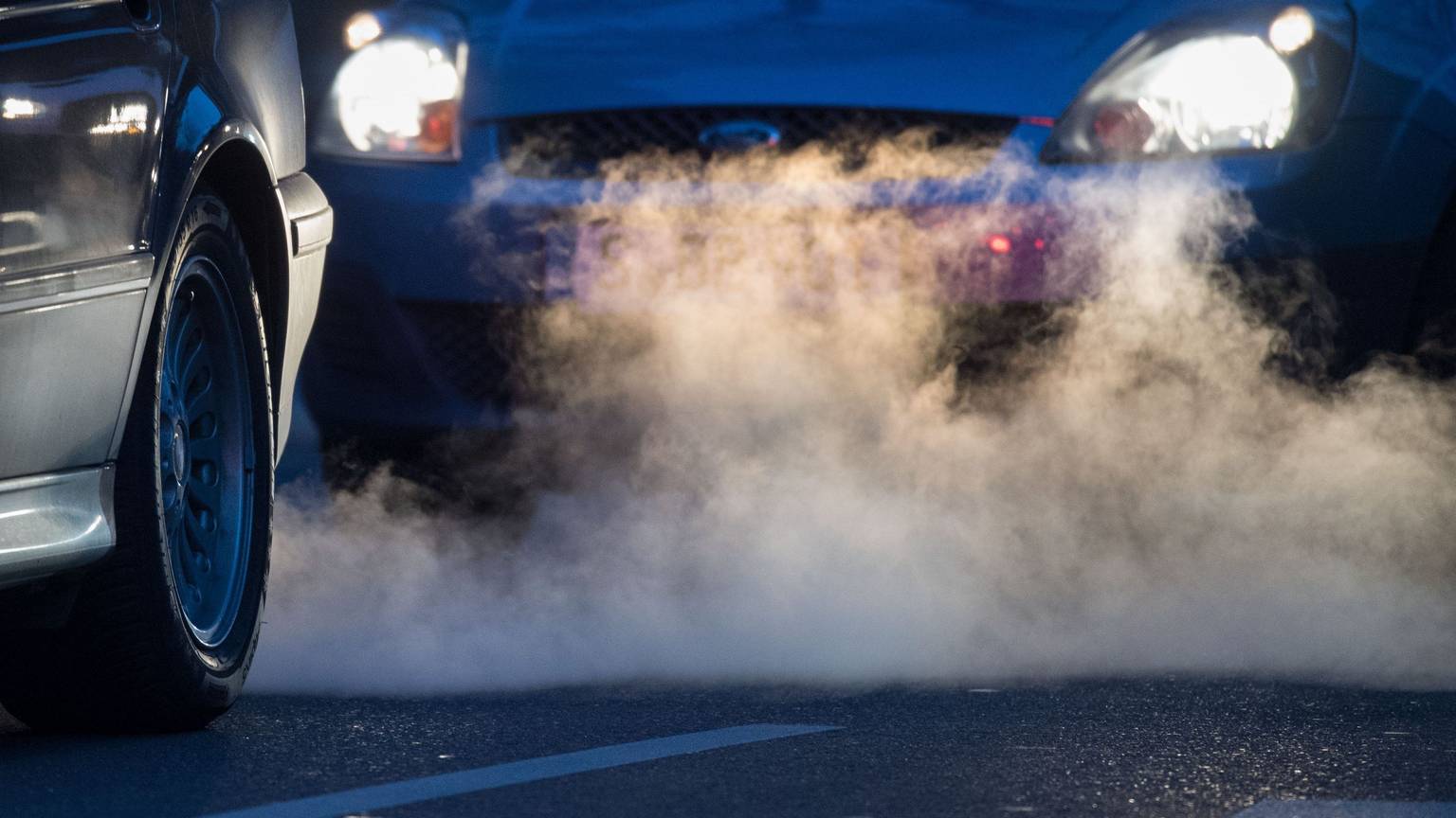 Zwei Autos stehen hintereinander. Aus dem vorderen Auspuff kommt Qualm raus.