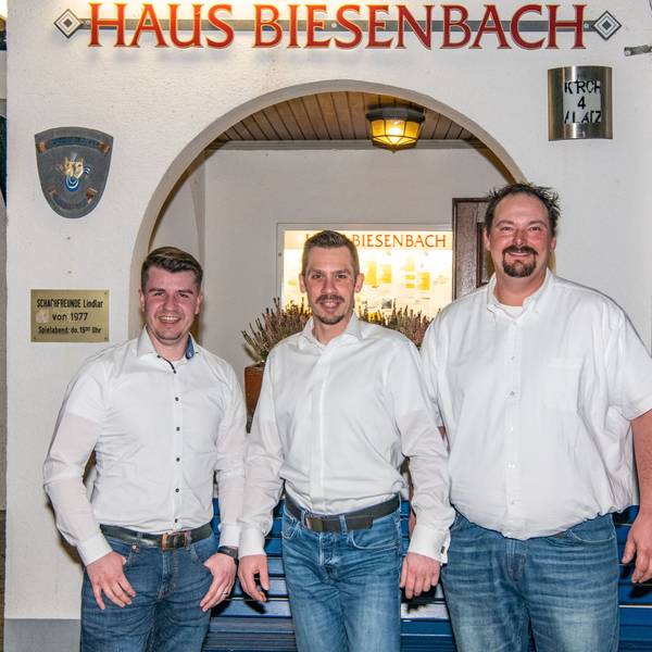 Die drei Männer stehen vor einer Mauer mit einem Torbogen.