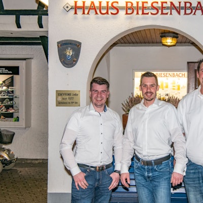 Die drei Männer stehen vor einer Mauer mit einem Torbogen.