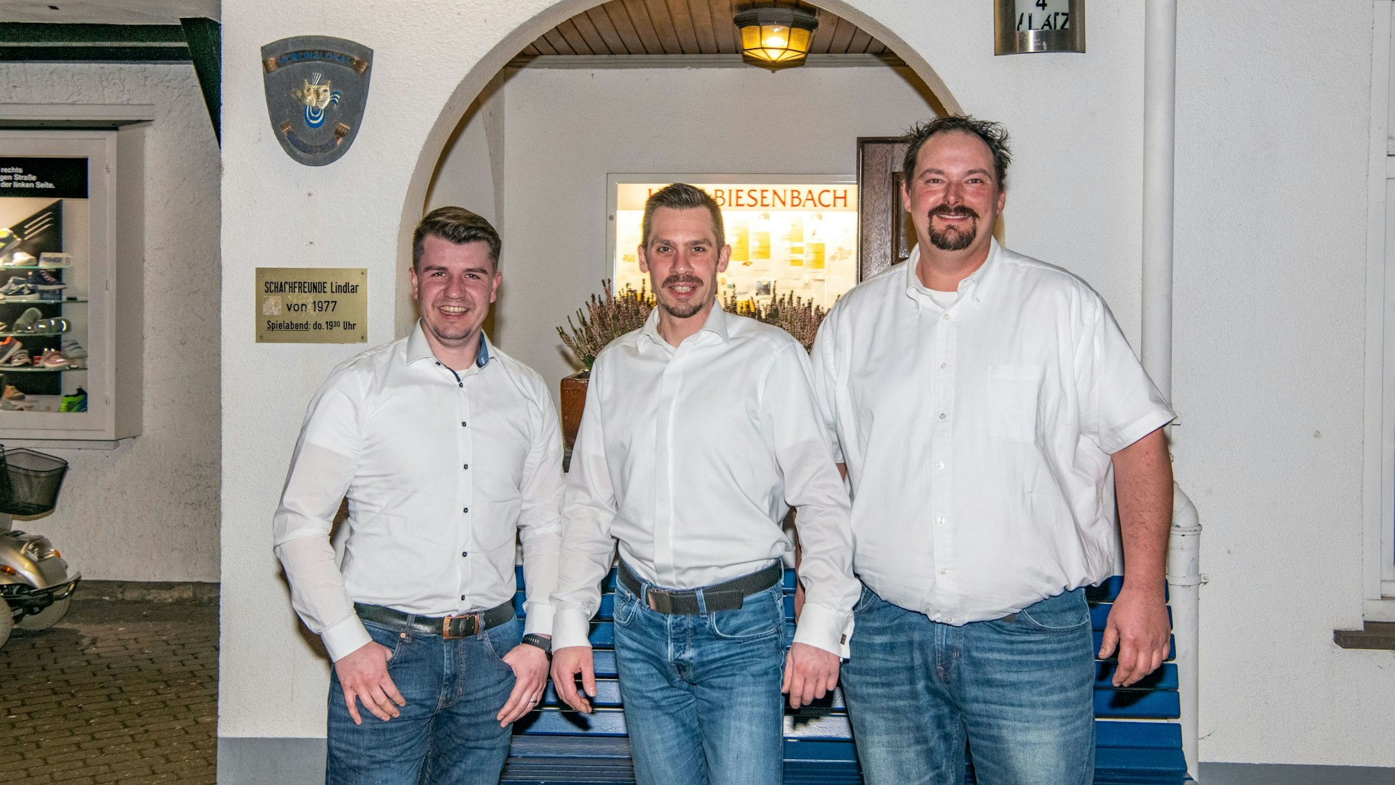 Die drei Männer stehen vor einer Mauer mit einem Torbogen.